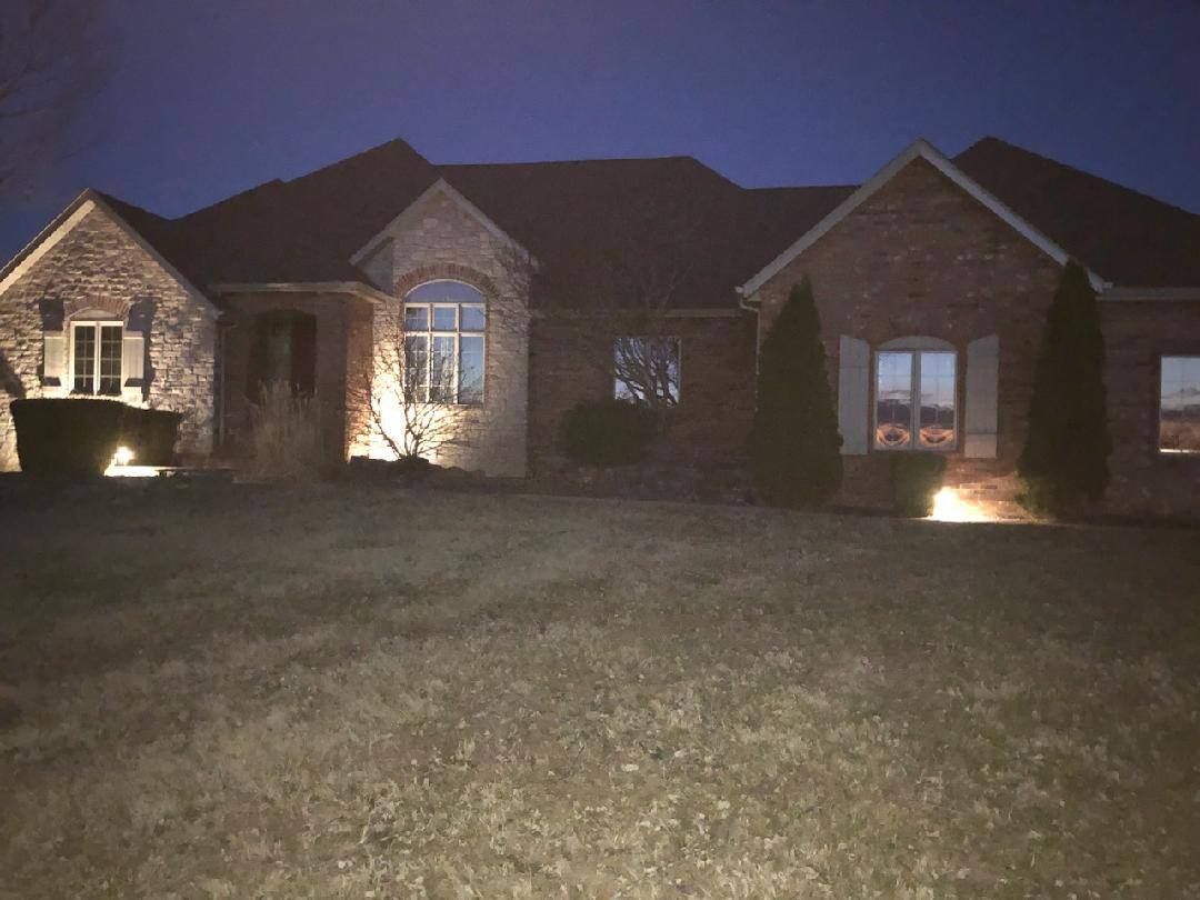 Brick house at night, illuminated by spotlights, with a dark sky and a grassy lawn.