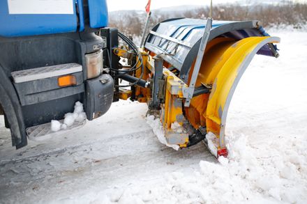 Snowplow blade clearing snow beside a blue truck on a snowy road