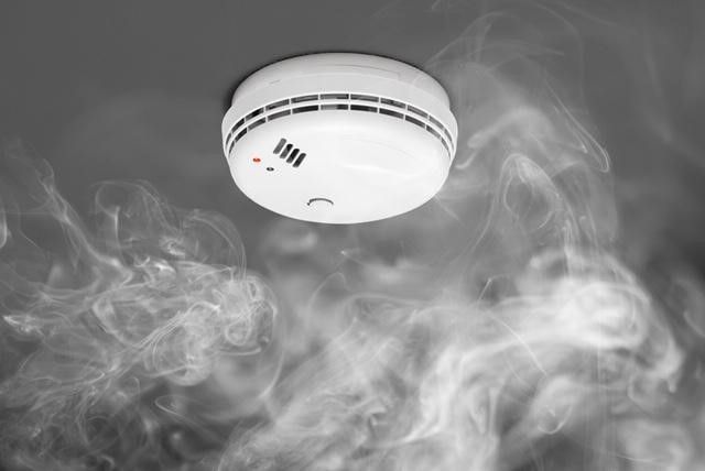 A smoke detector is surrounded by smoke in a room.
