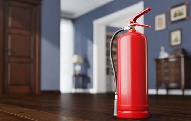A red fire extinguisher is sitting on a wooden floor in a living room.