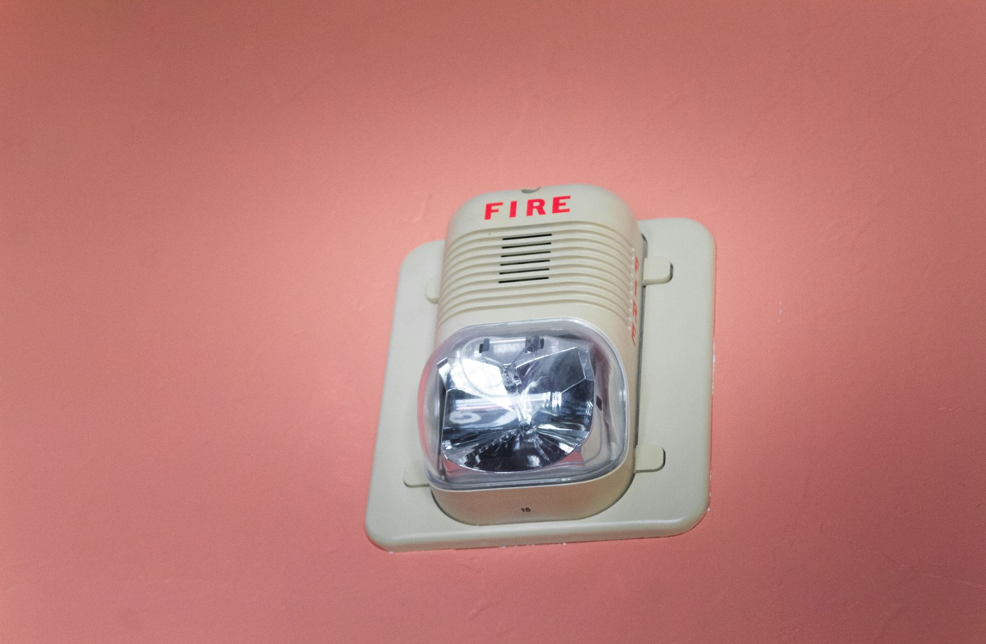 A fire alarm is mounted on a pink wall.