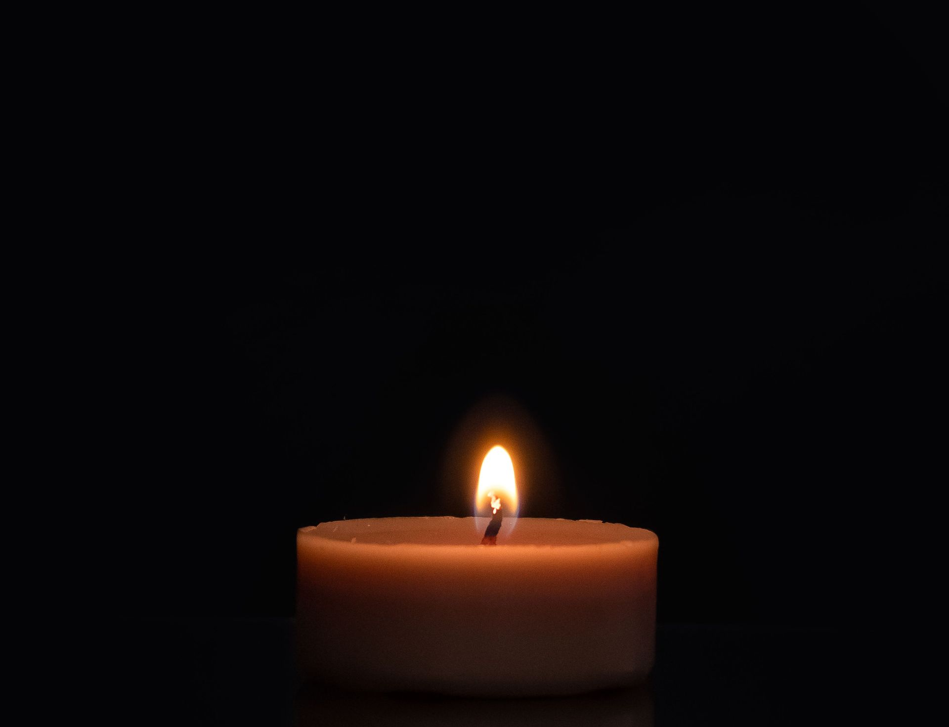 Lit candle reflected in a dark, mirror-like surface