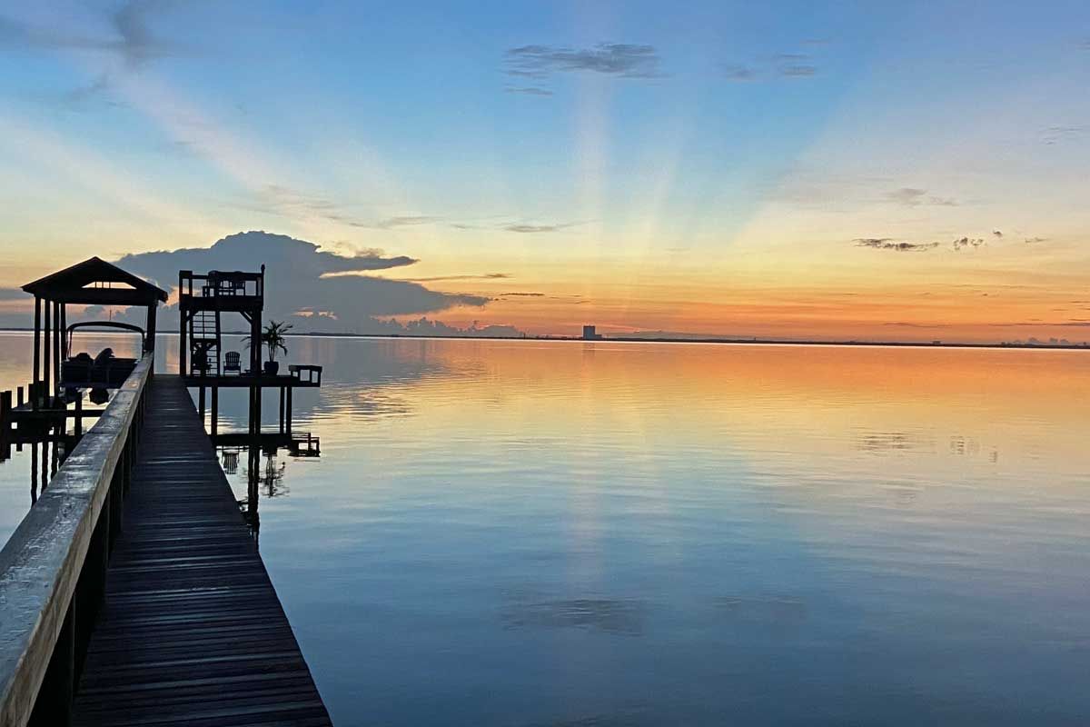 Sunrise over calm water with a wooden dock and small gazebo silhouettes