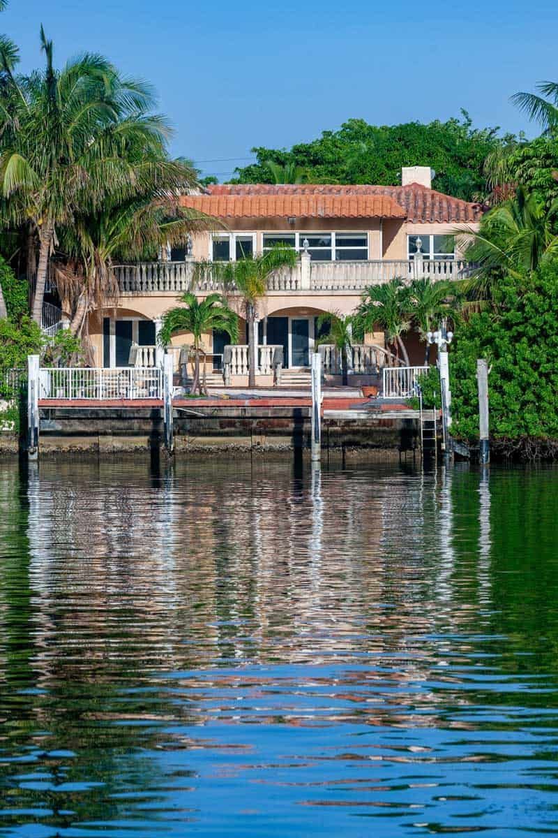 Waterfront house with red roof and palm trees reflecting on calm water