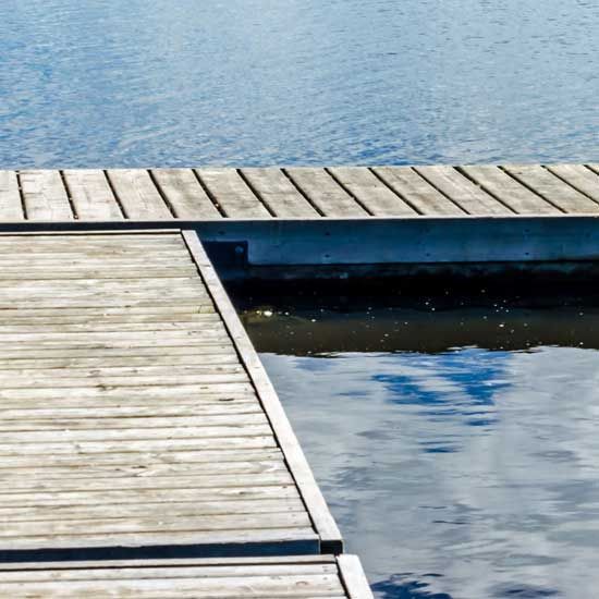 Wooden dock beside calm blue water, with reflections and a slanted platform in the foreground