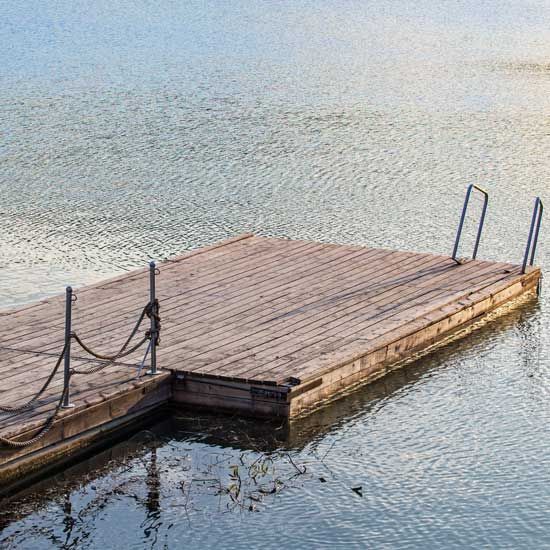 Wooden dock floating on calm water, with metal ladder rails at the right end.