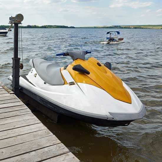 Yellow and white jet ski tied to a dock on a lake, with another jet ski in the distance.