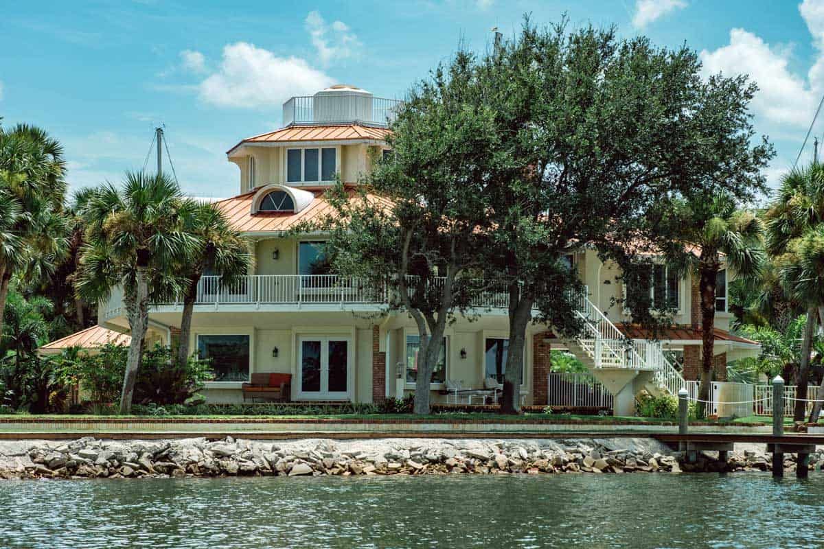 Waterfront house with a tower, palm trees, and a dock beside calm water