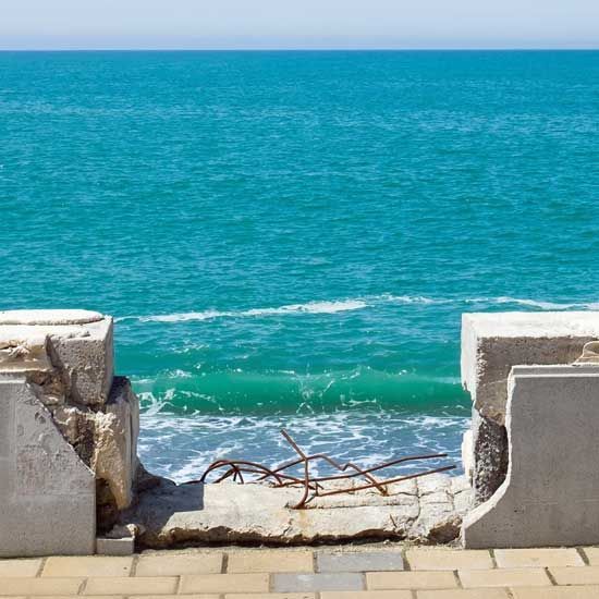 View through a broken stone opening to turquoise ocean and a small crashing wave