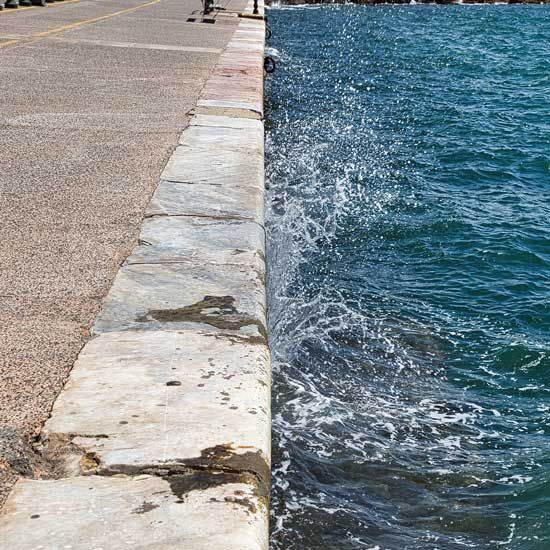 Seaside walkway with a low stone edge beside choppy blue water