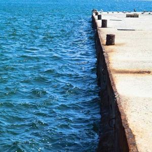 Blue water waves next to a concrete seawall with dark, weathered bollards.