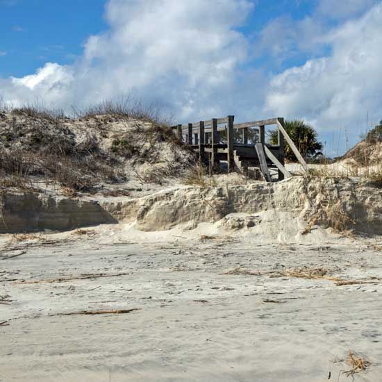 Sandy beach dunes with a wooden walkway under a partly cloudy blue sky
