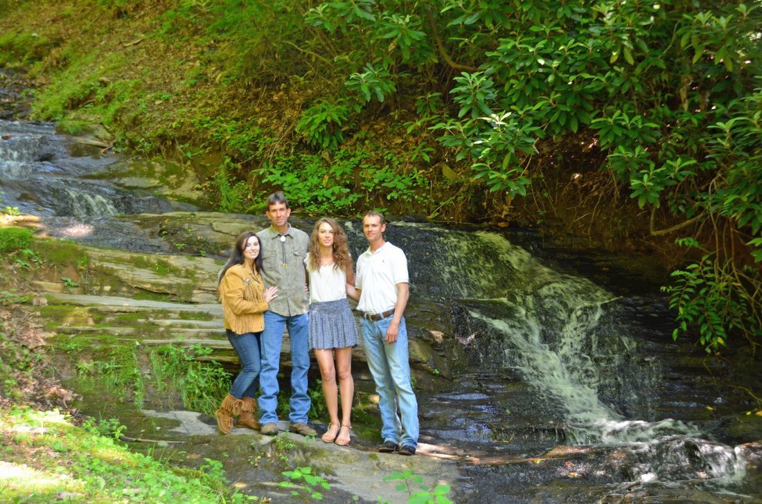 Four people standing by a small waterfall in a lush green forest