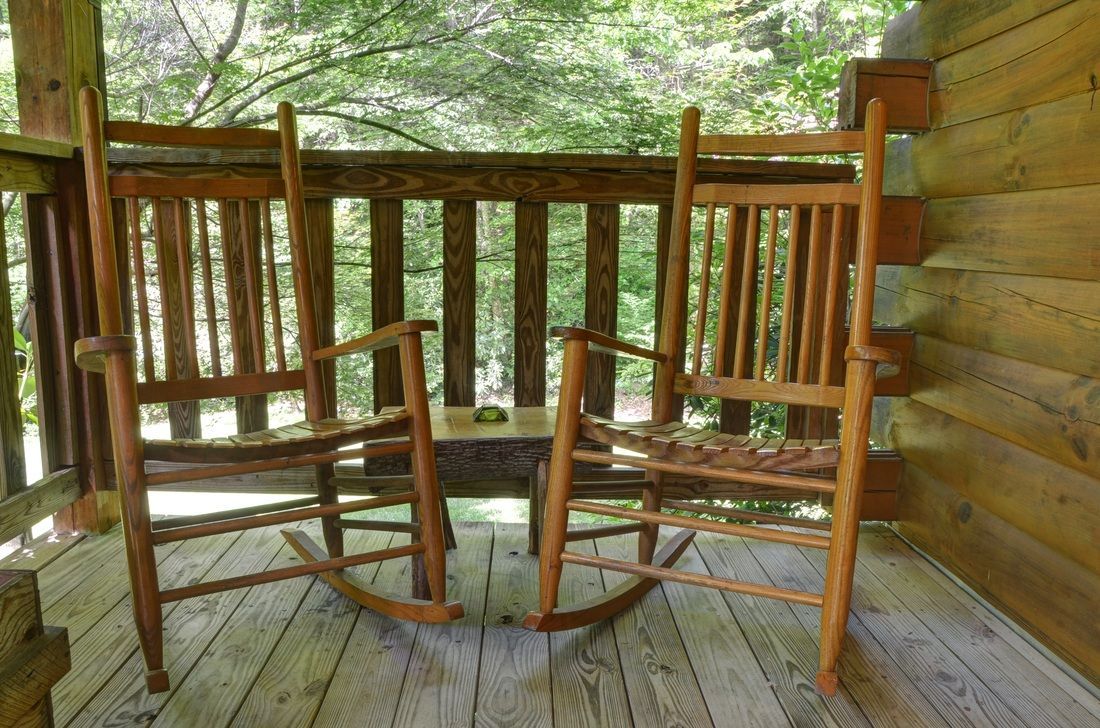 Two wooden rocking chairs on a cabin porch overlooking a wooded forest.