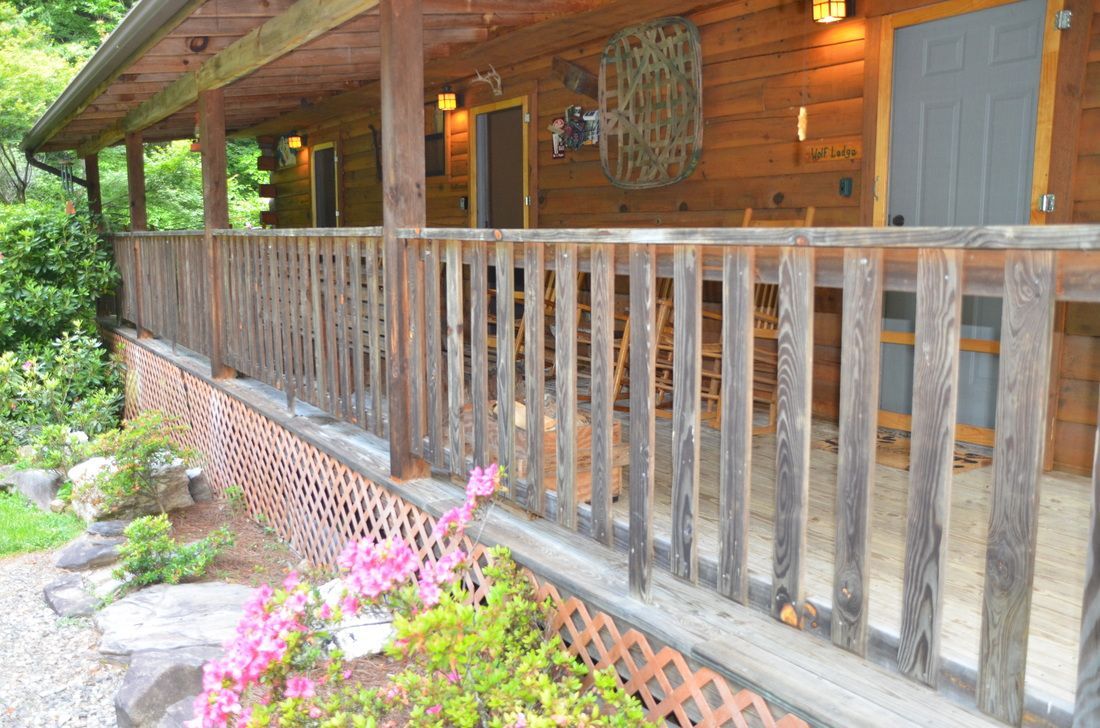 Wooden cabin porch with railing, stone path, and pink flowers in the foreground