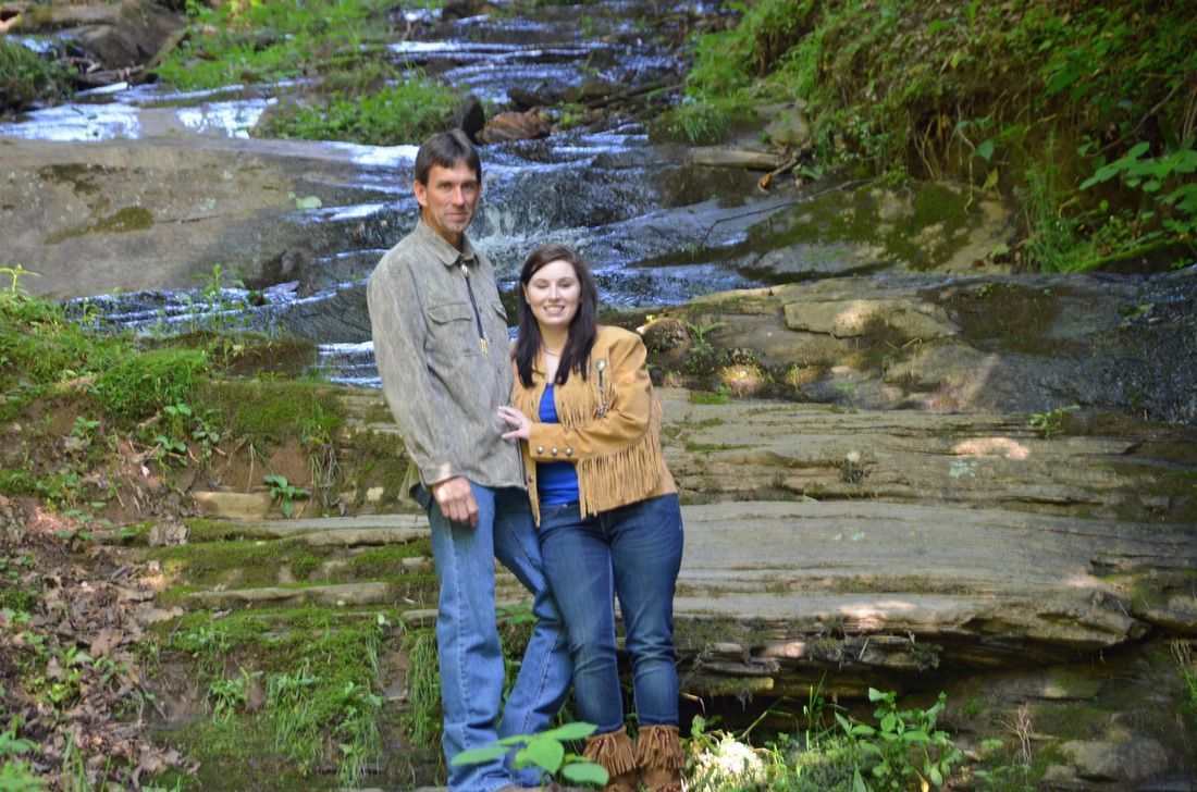 Couple standing on rocks by a small waterfall in a wooded creek