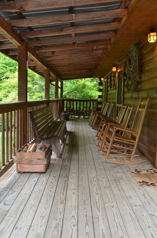 Wooden cabin porch with rocking chairs, bench, lanterns, and a rustic log wall.
