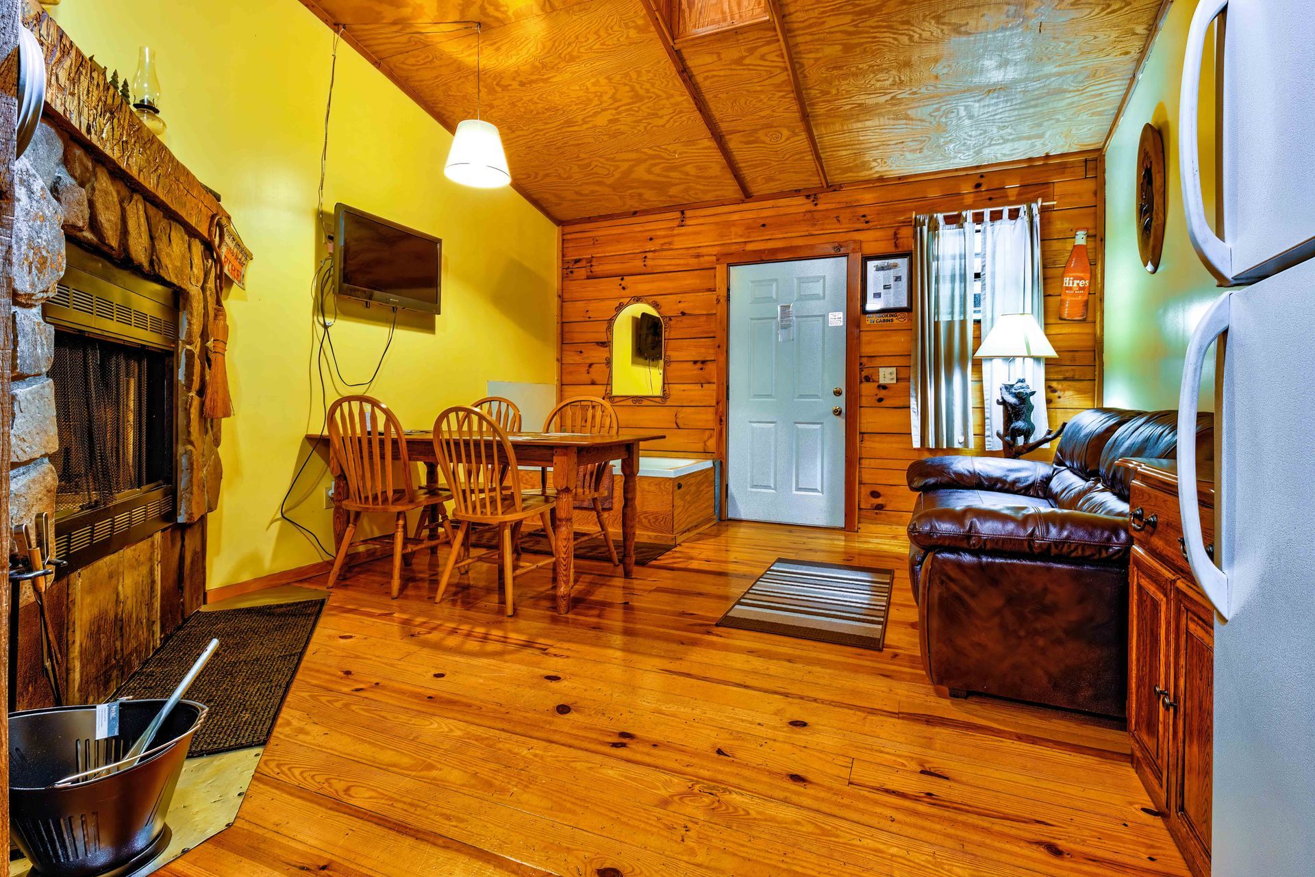 Cozy wood-paneled cabin interior with dining table, sofa, chairs, and white door under warm lighting