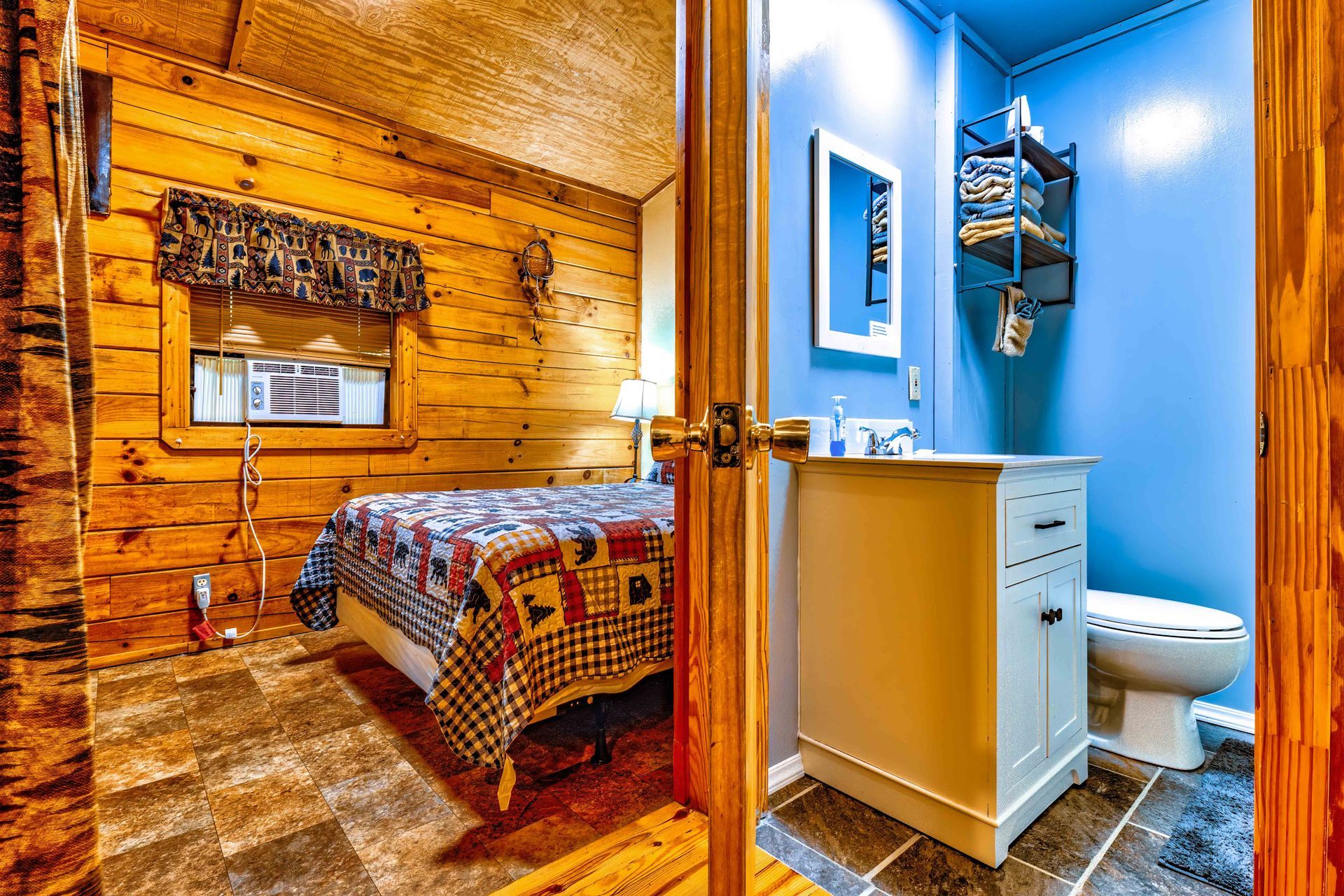 Rustic bedroom with log walls beside a bright blue bathroom with toilet and sink.