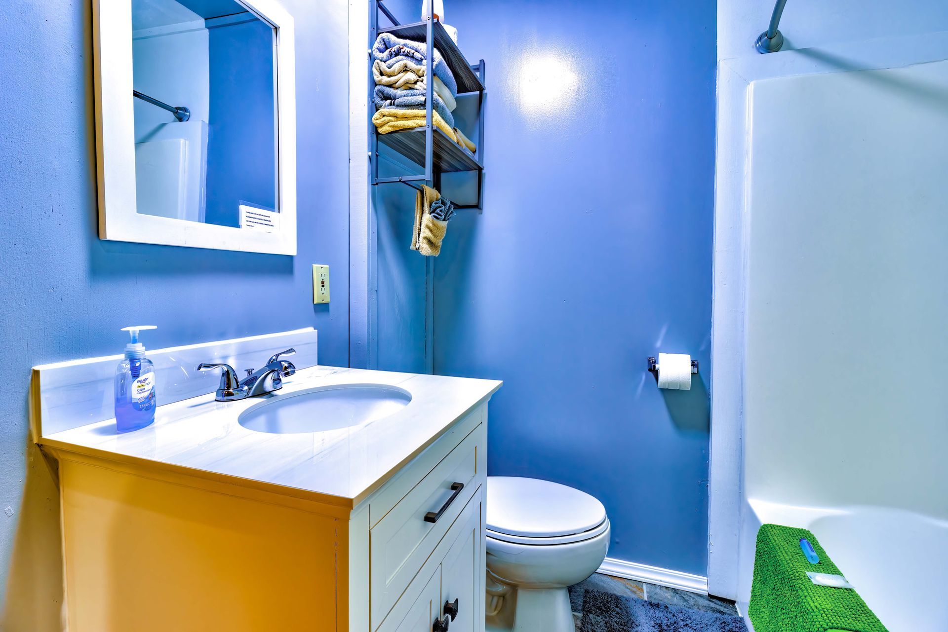Small blue bathroom with vanity, toilet, shower curtain, and wall shelf