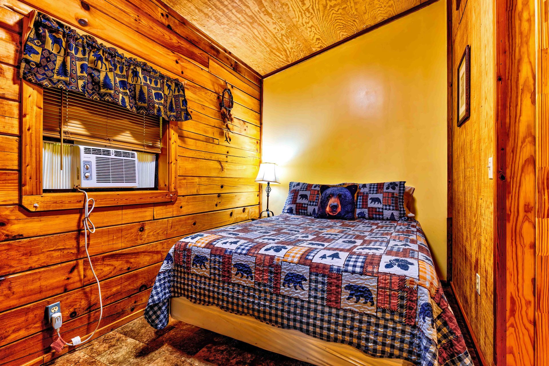 Rustic wood-paneled bedroom with a quilted bed, yellow wall, and window air conditioner