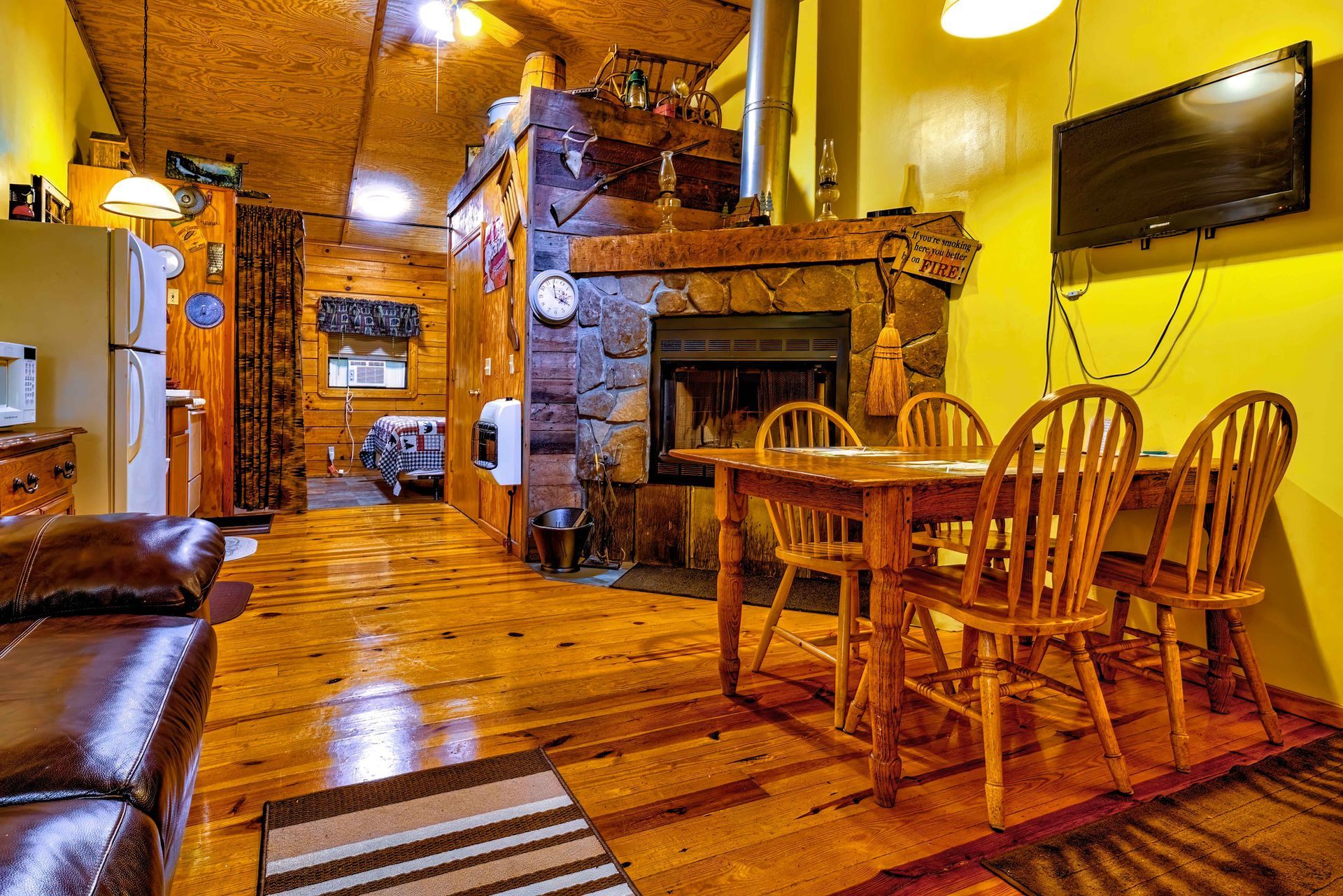 Cozy rustic dining room with wooden table, chairs, stone fireplace, and warm yellow lighting