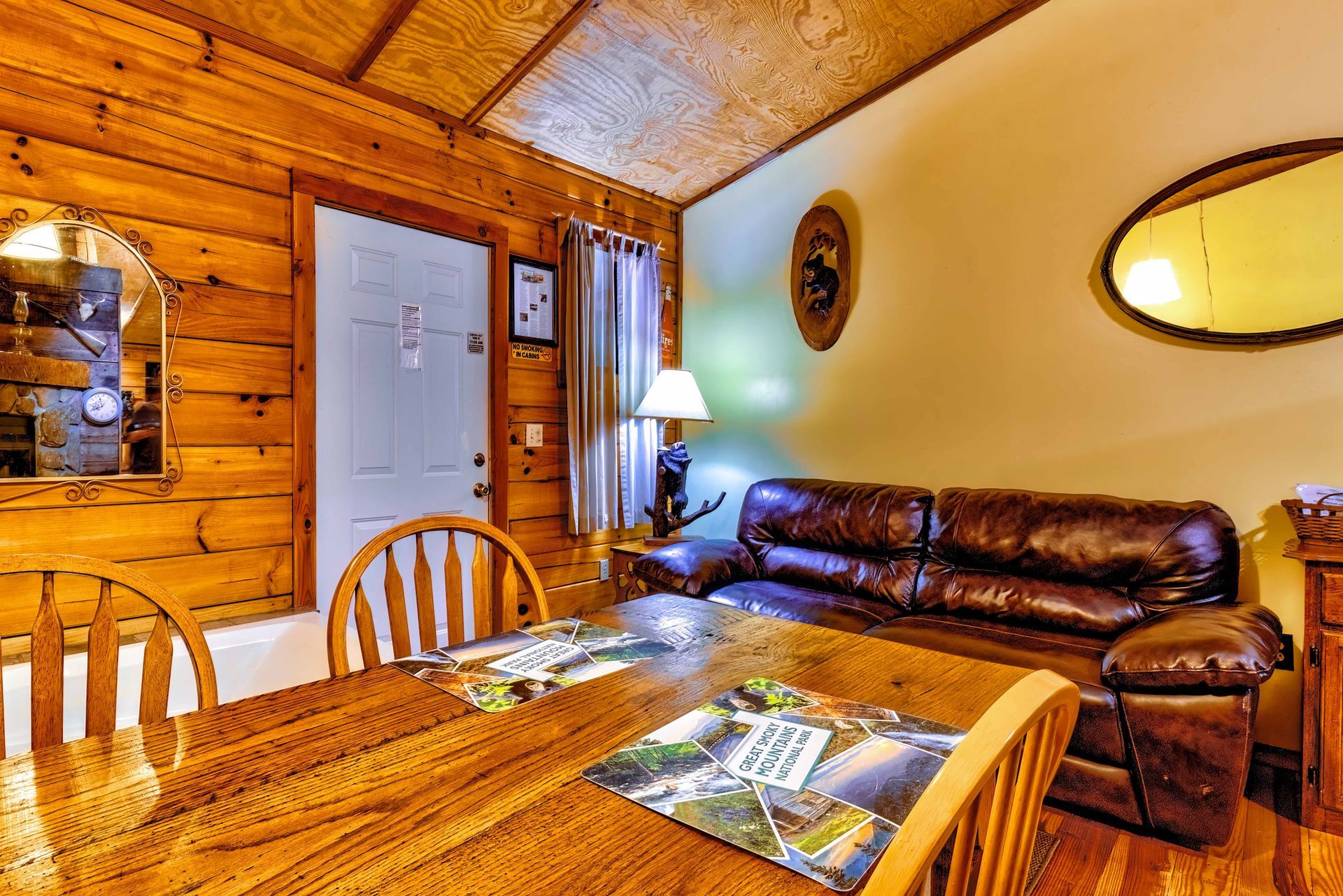 Cozy cabin living room with wood-paneled walls, leather sofa, dining table, and warm lighting