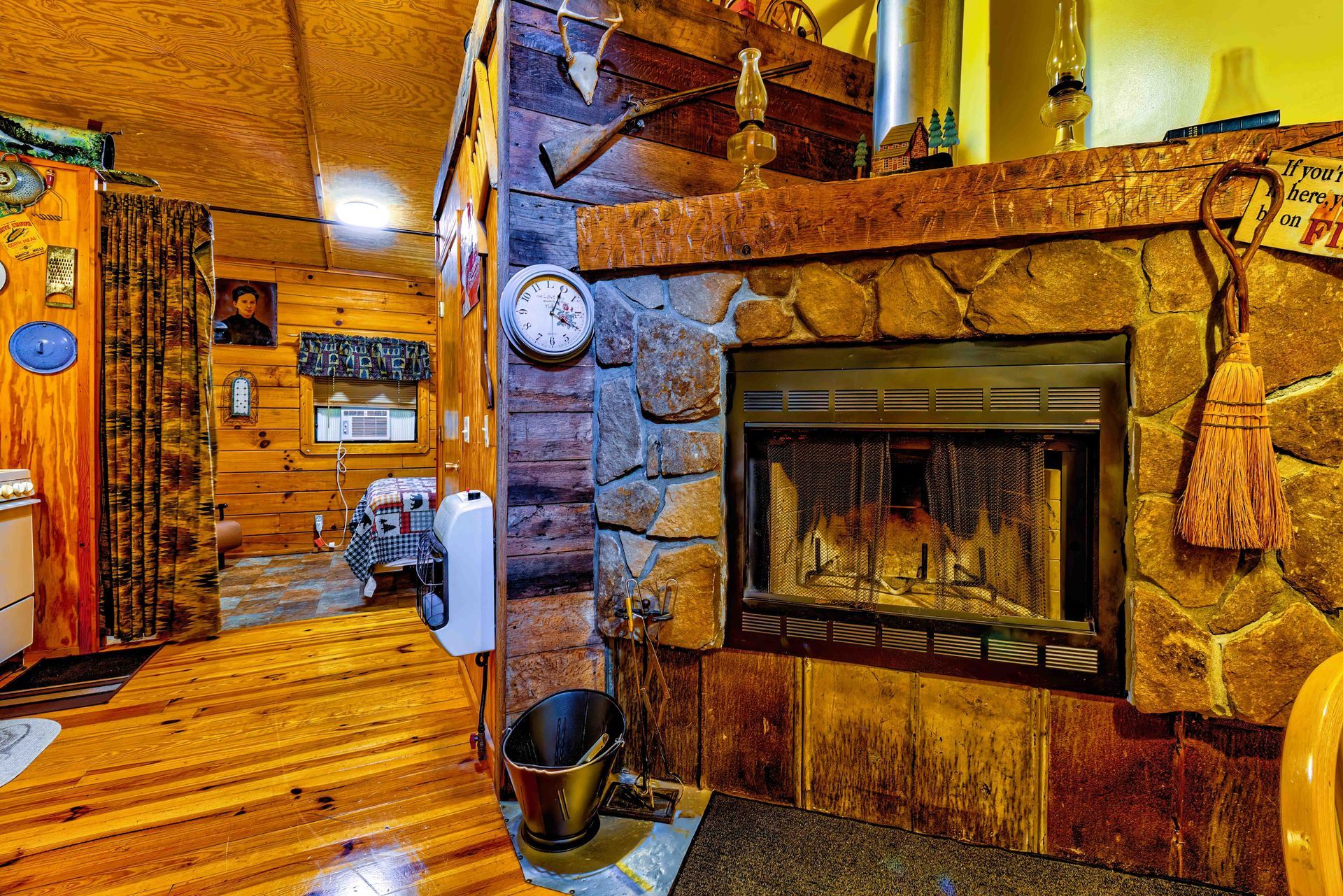 Cozy rustic living room with a stone fireplace, wooden walls, and warm yellow lighting.