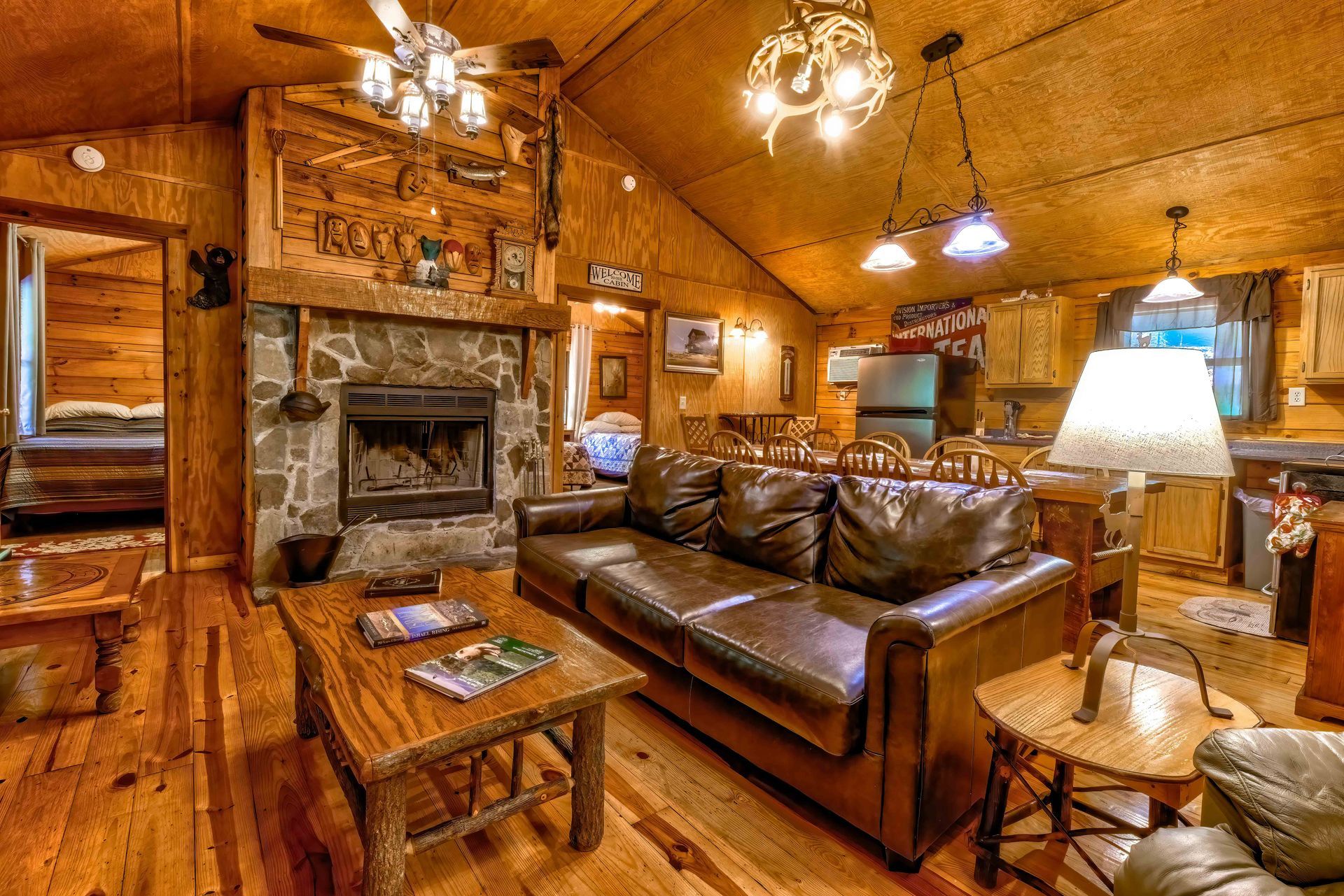 Rustic wood-paneled living room with leather sofa, fireplace, coffee table, and warm lamps