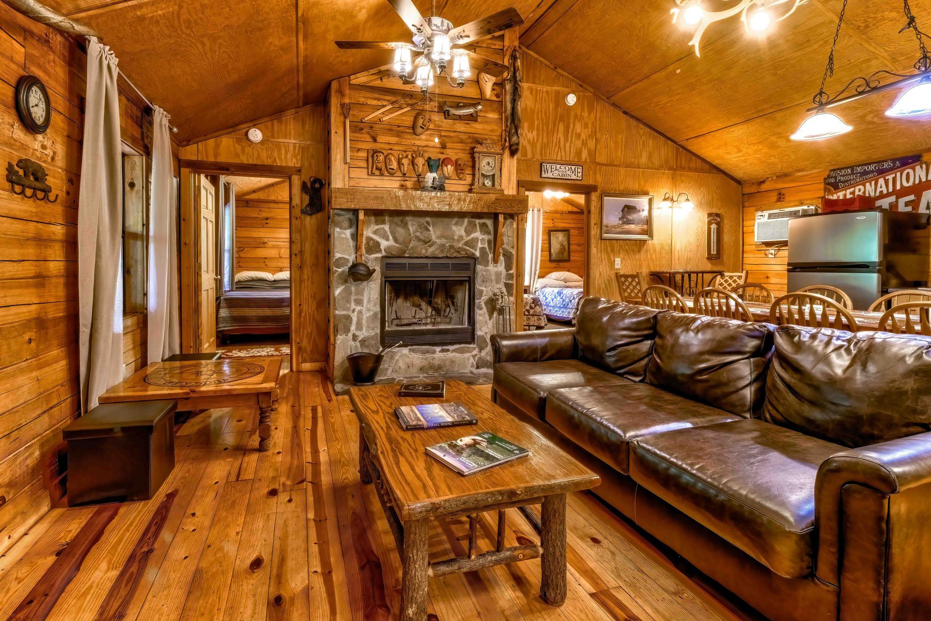 Cozy rustic cabin living room with leather sectional, stone fireplace, wooden walls, and warm lighting