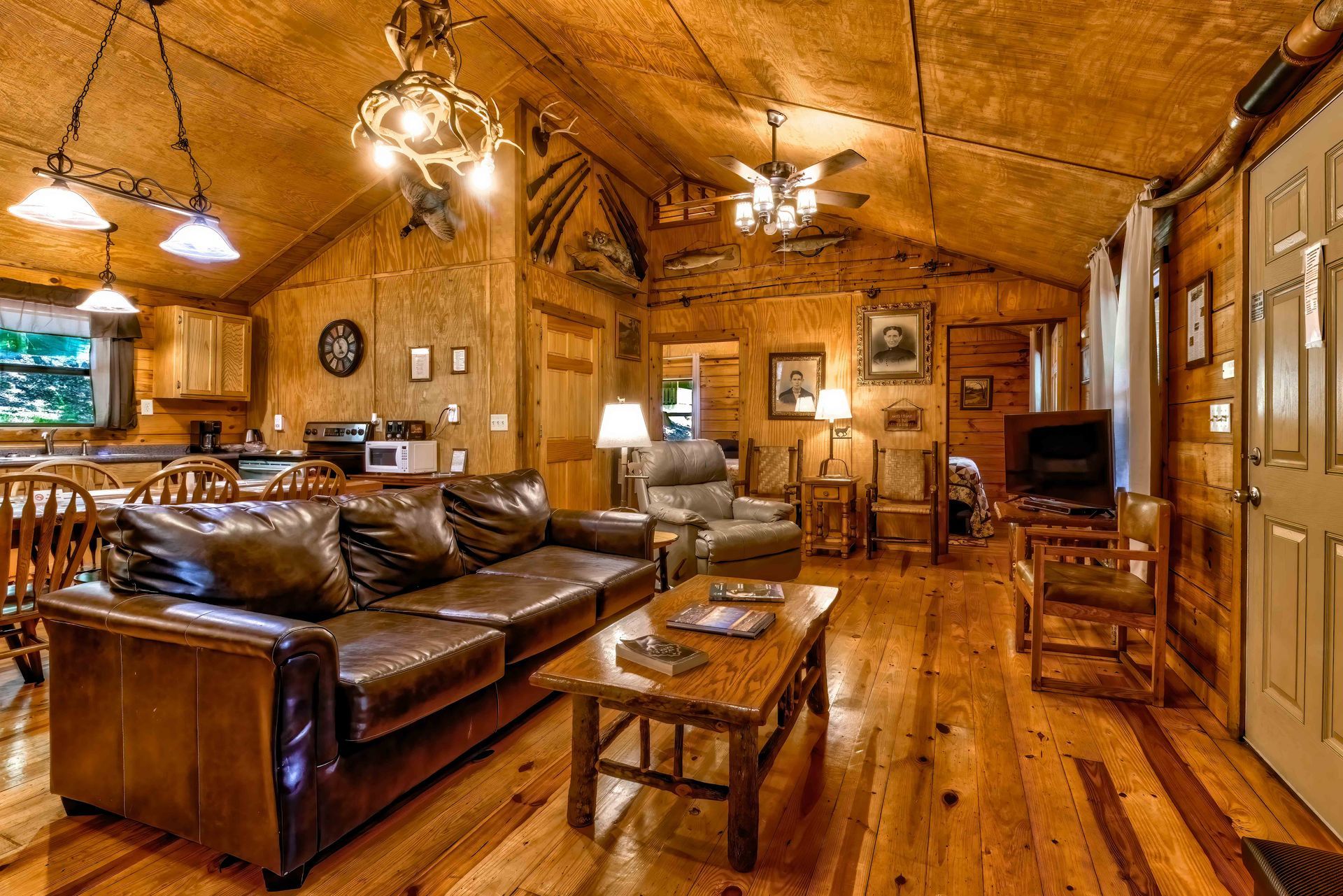 Cozy rustic living room with brown leather sofas, wooden walls, warm lighting, and a polished wood floor