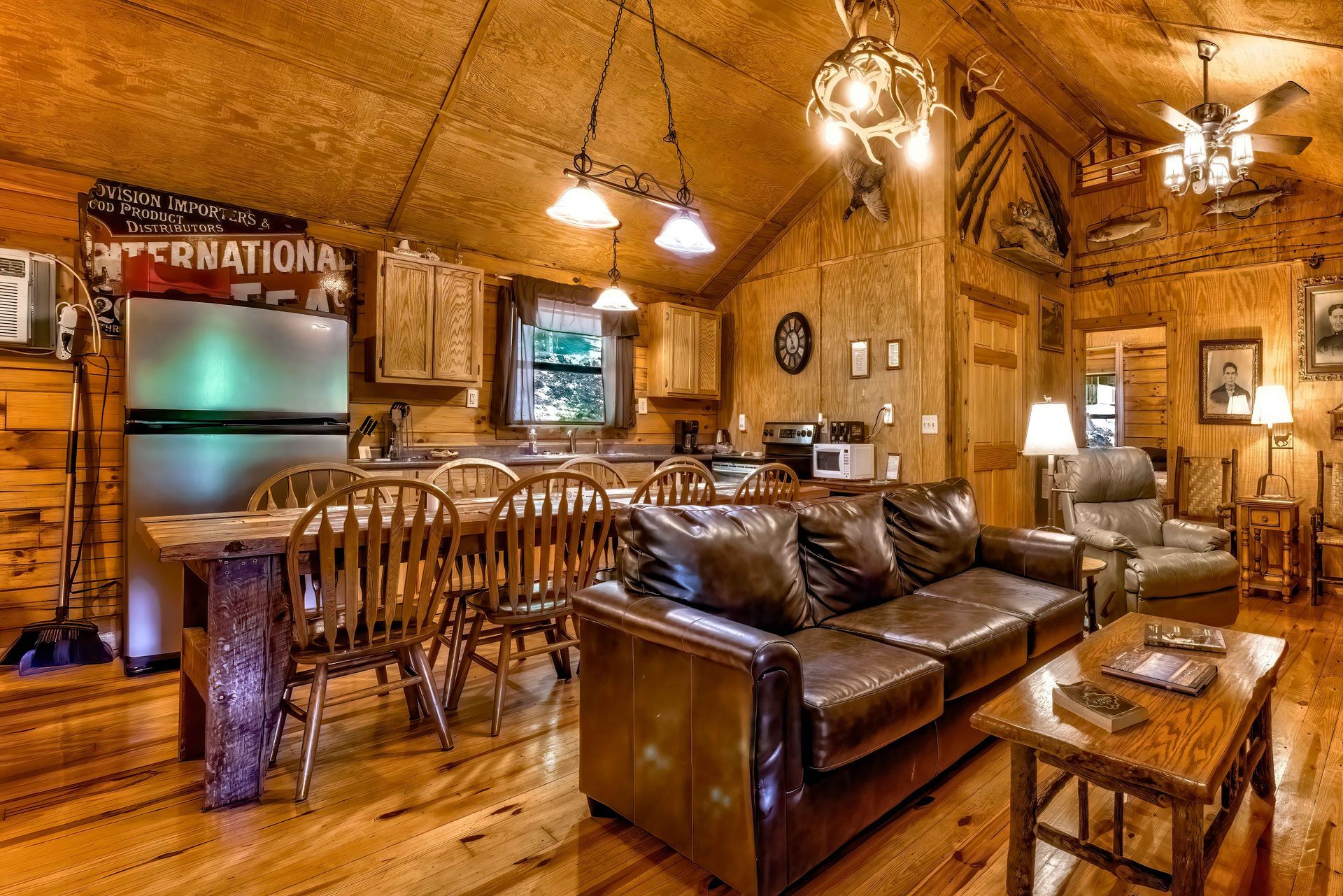 Rustic cabin-style living room with leather sofas, wood walls, and warm pendant lighting