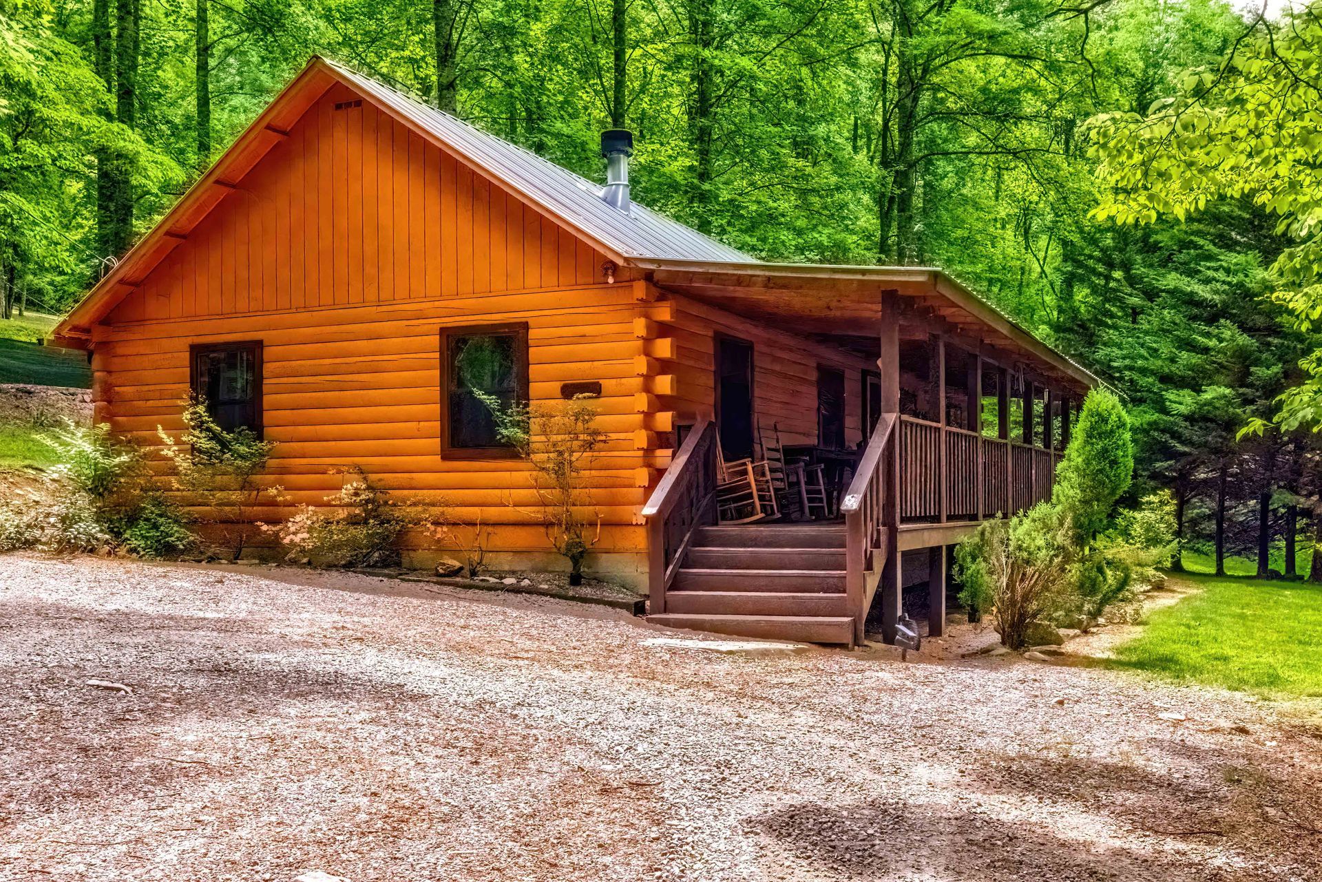 Orange log cabin with porch and steps in a wooded forest clearing