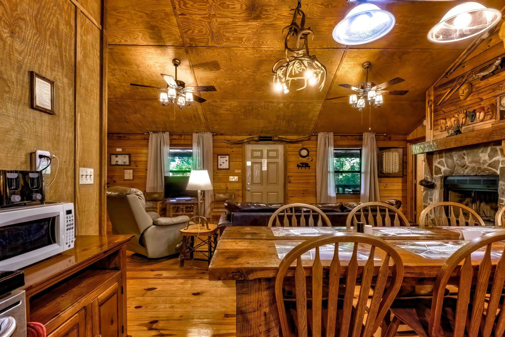 Rustic cabin-style kitchen and dining room with wooden walls, table, chairs, and ceiling lights.