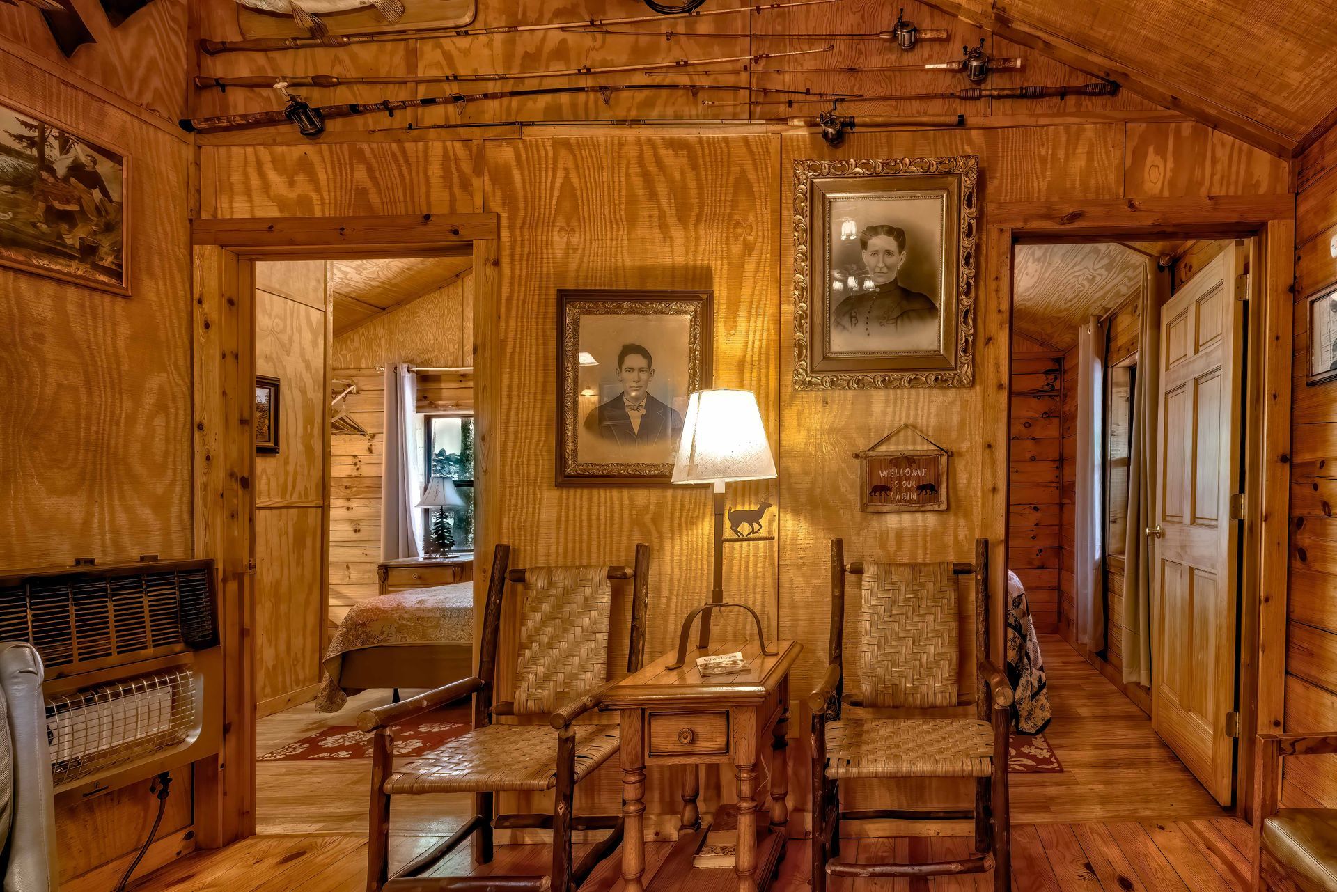 Warm wood-paneled cabin room with vintage furniture, lamp, rocking chair, and framed portraits