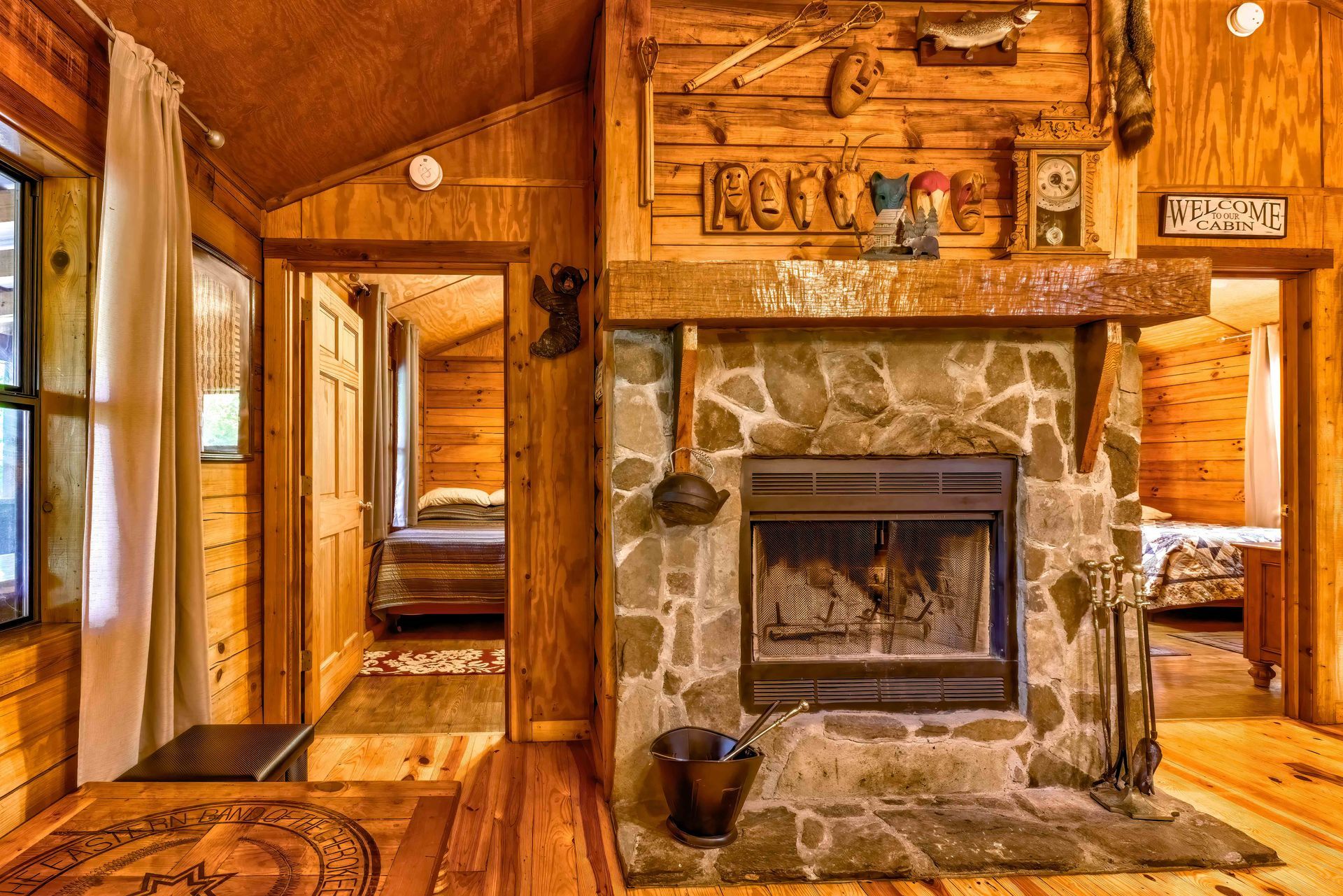 Rustic wood-paneled cabin interior with stone fireplace, hallway, and warm amber lighting