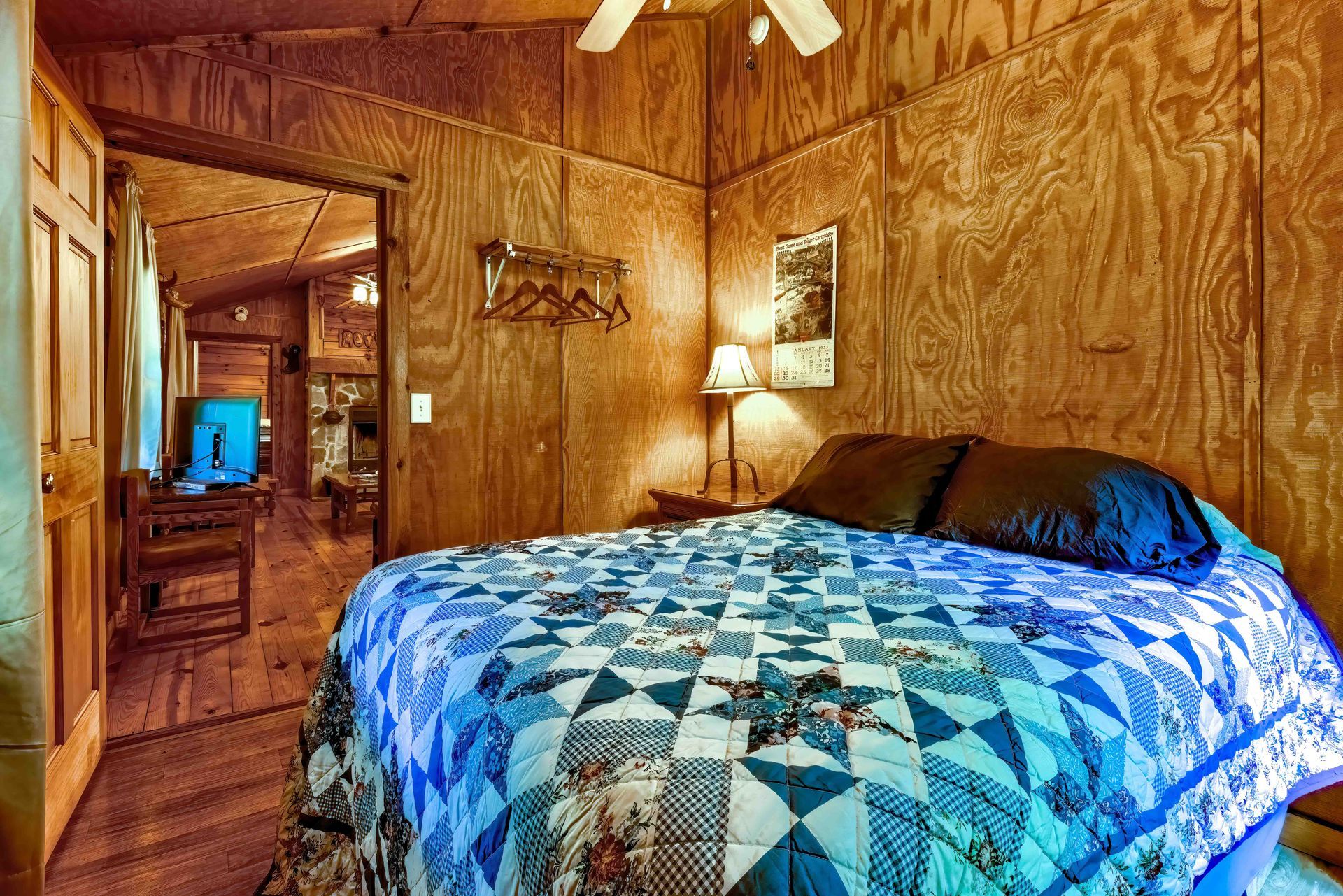 Rustic wood-paneled bedroom with a blue patchwork quilt and warm lamp lighting
