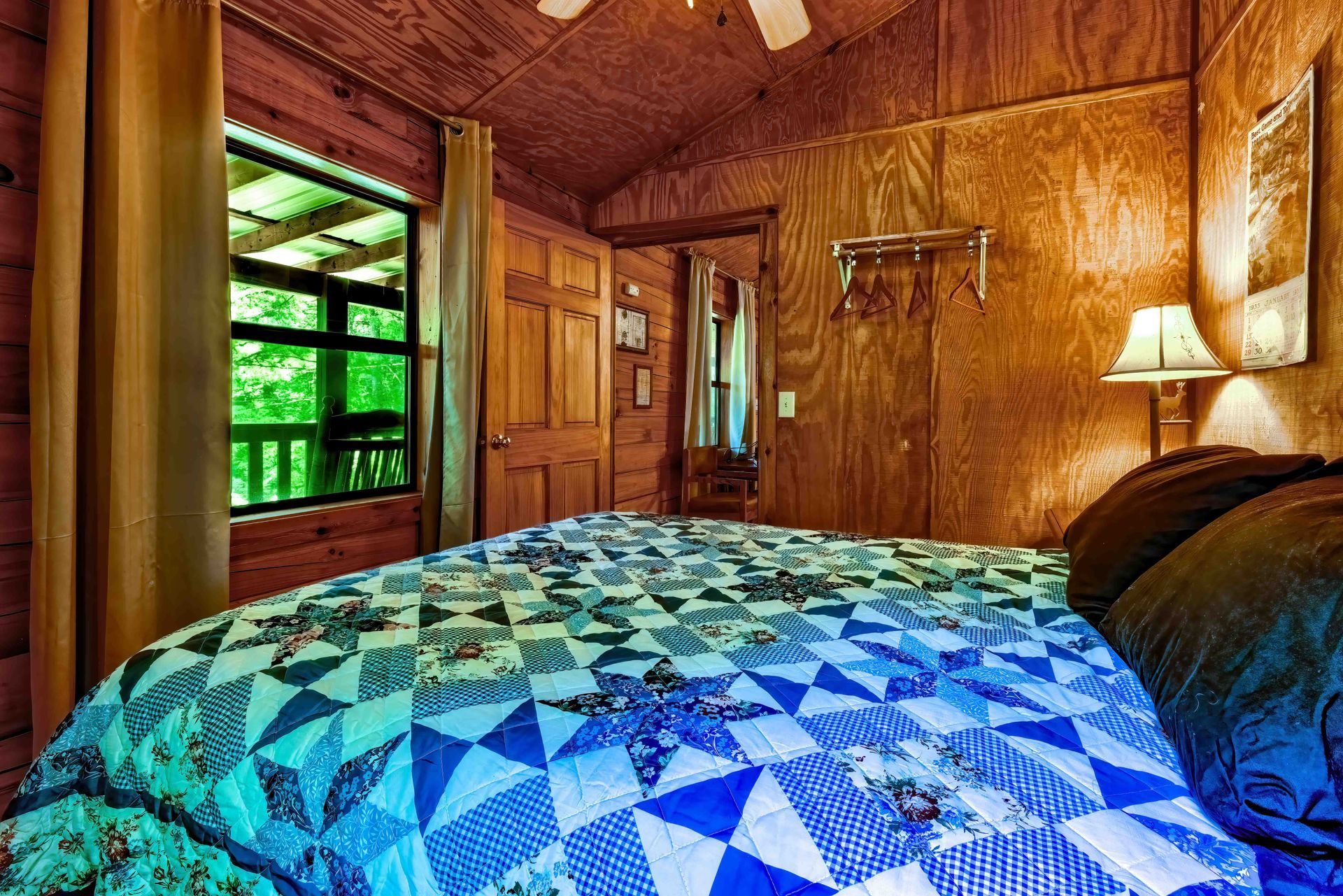 Cozy wood-paneled cabin bedroom with quilted bed, window view, and bedside lamp