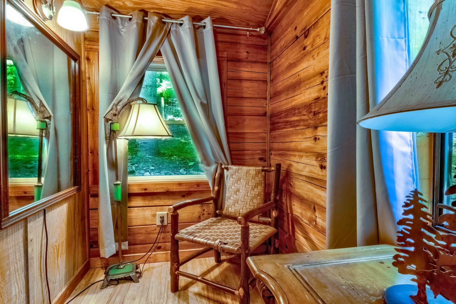 Cozy wood-paneled nook with a window seat, armchair, lamp, and sheer curtains overlooking greenery