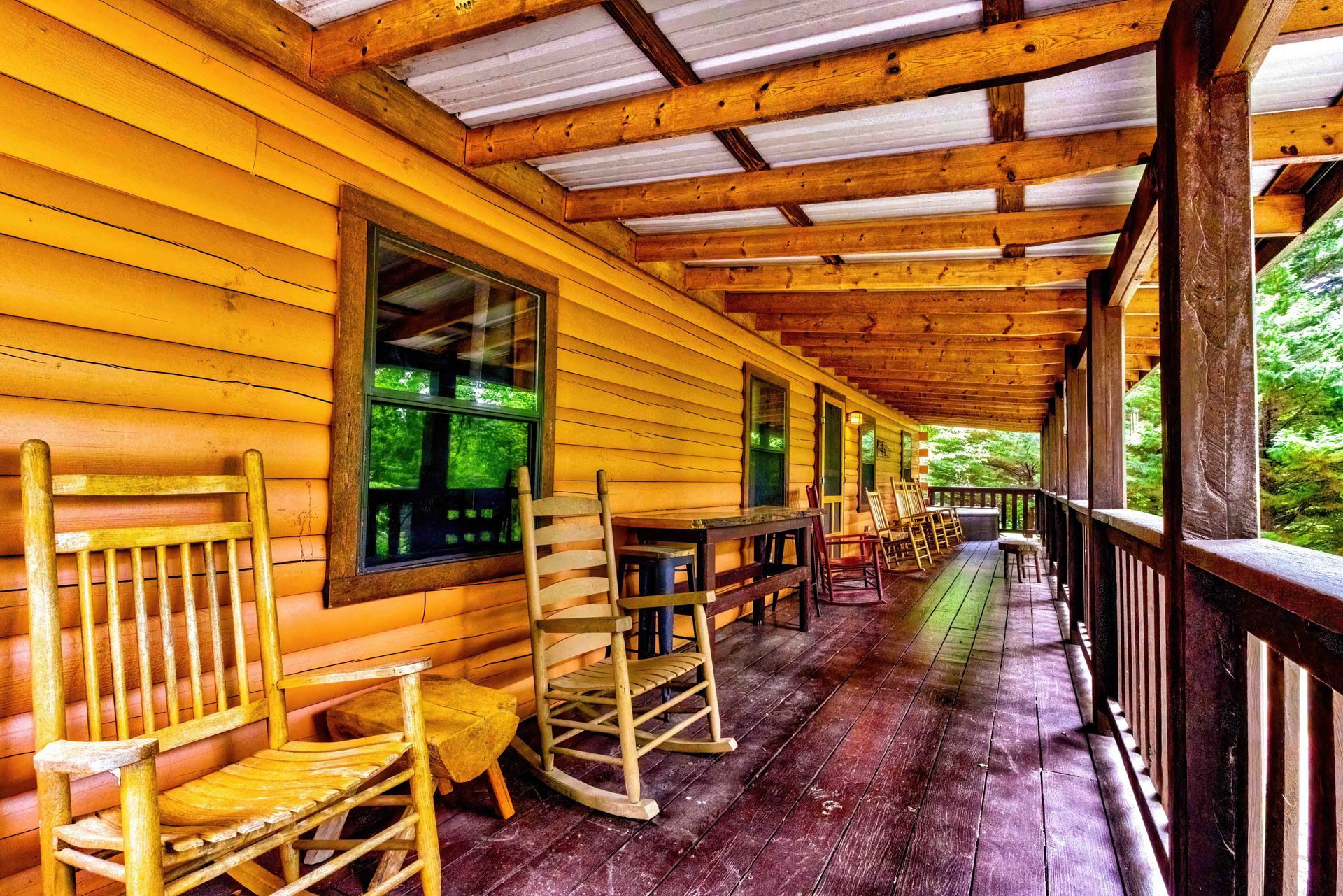 Wooden cabin porch with rocking chairs, table, and a long covered walkway overlooking trees