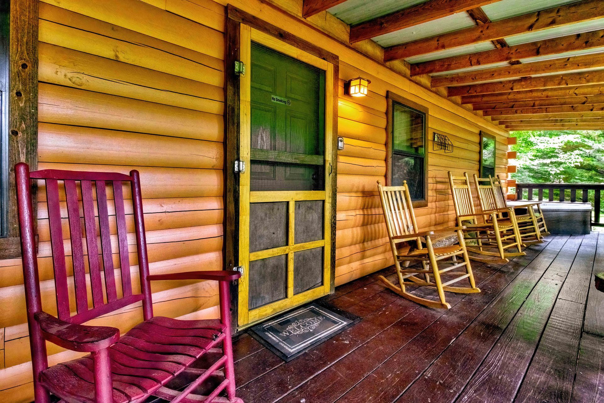 Log cabin porch with colorful rocking chairs, a green door, and wooden deck.