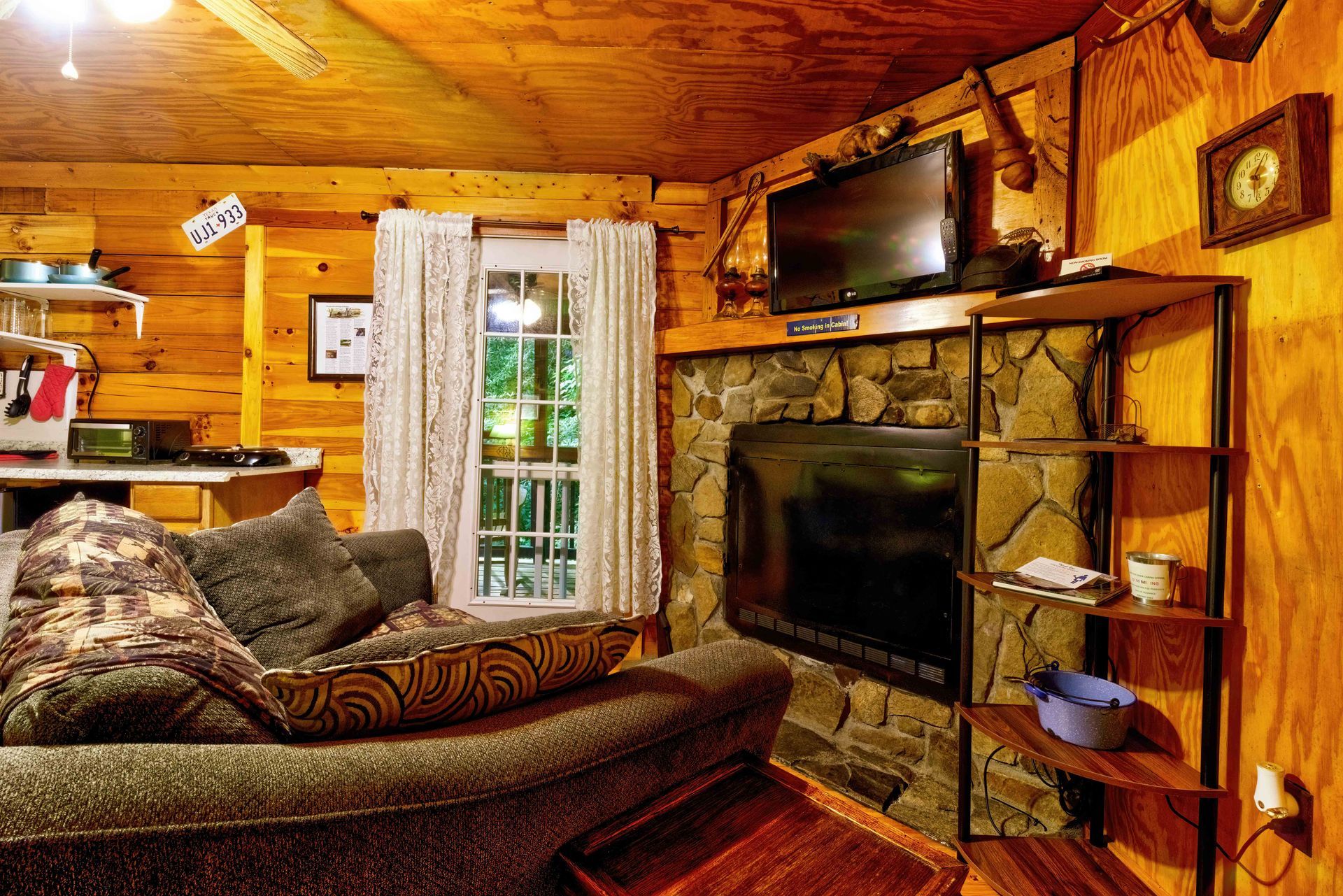 Rustic living room with leather sofa, stone fireplace, TV, and wood-paneled walls