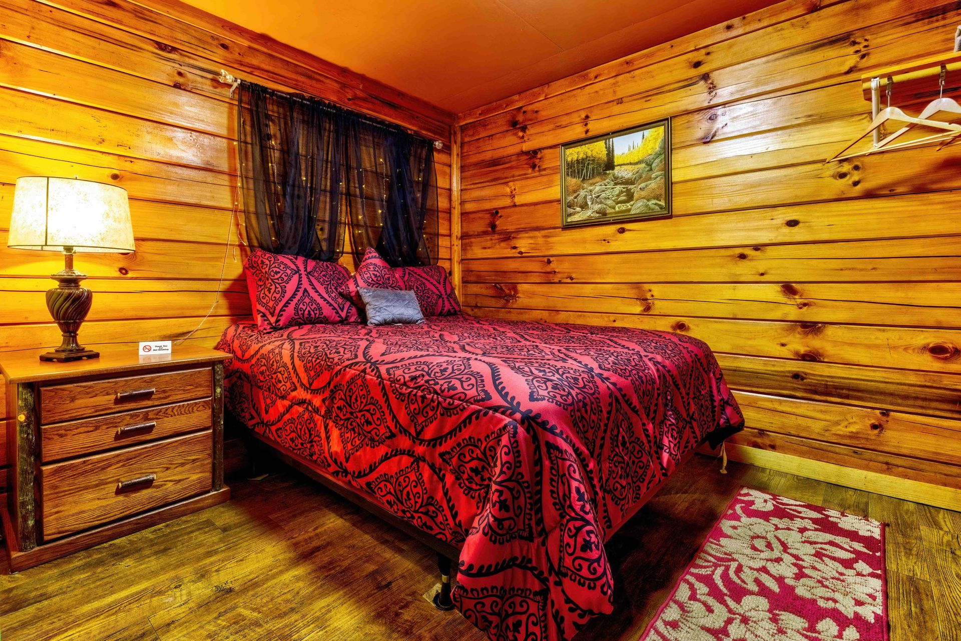 Cozy log cabin bedroom with a red bedspread, lamp-lit nightstand, and wood-paneled walls