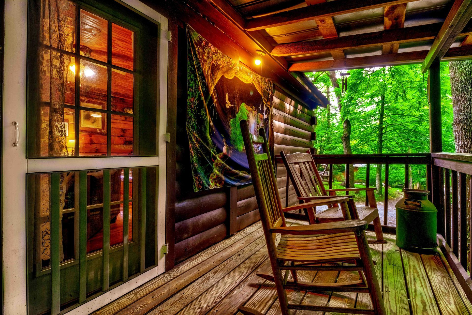 Wooden cabin porch with rocking chairs, a glowing lamp, and green forest view through the railing