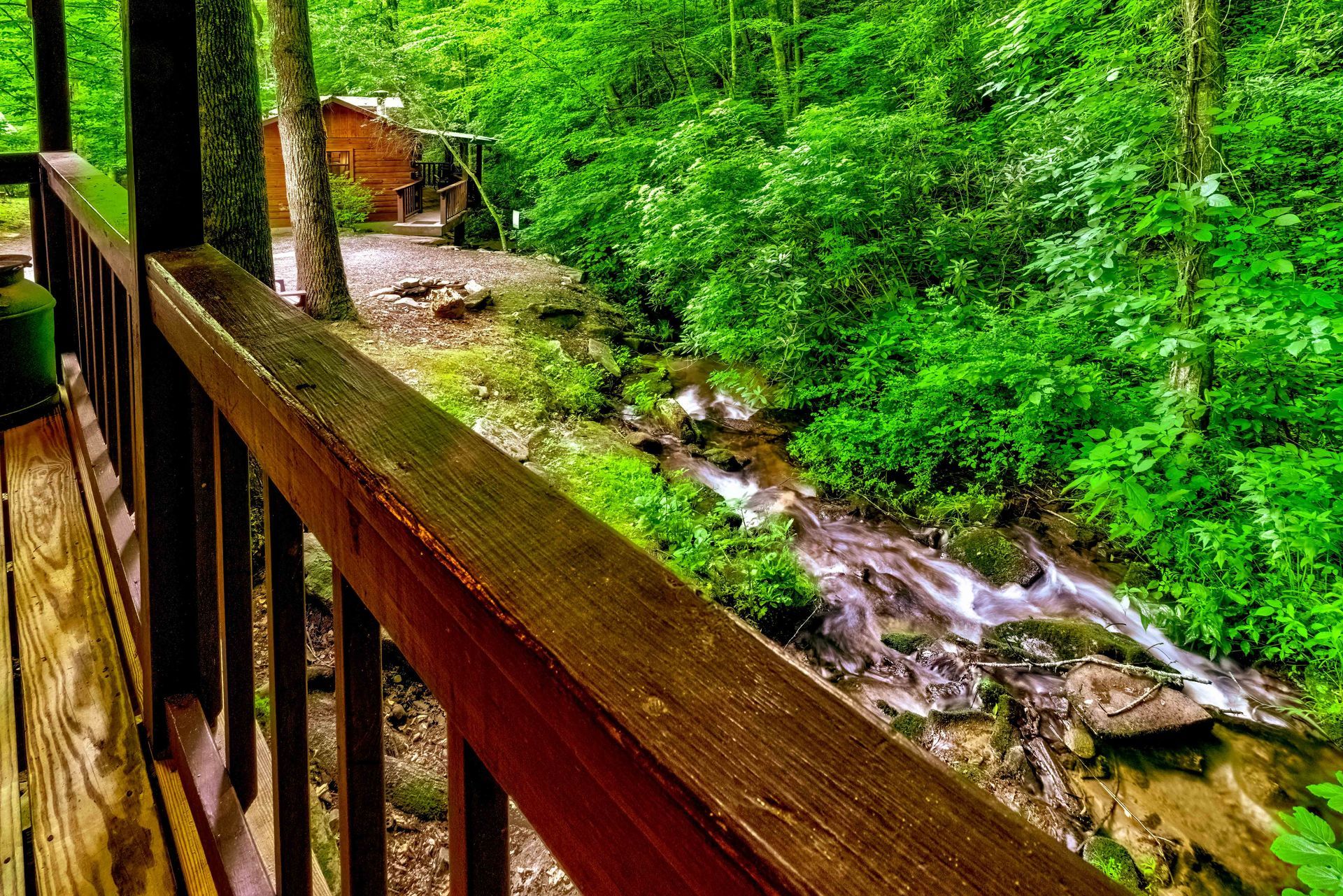 Wooden railing along a forest boardwalk beside a rocky stream in lush green woods