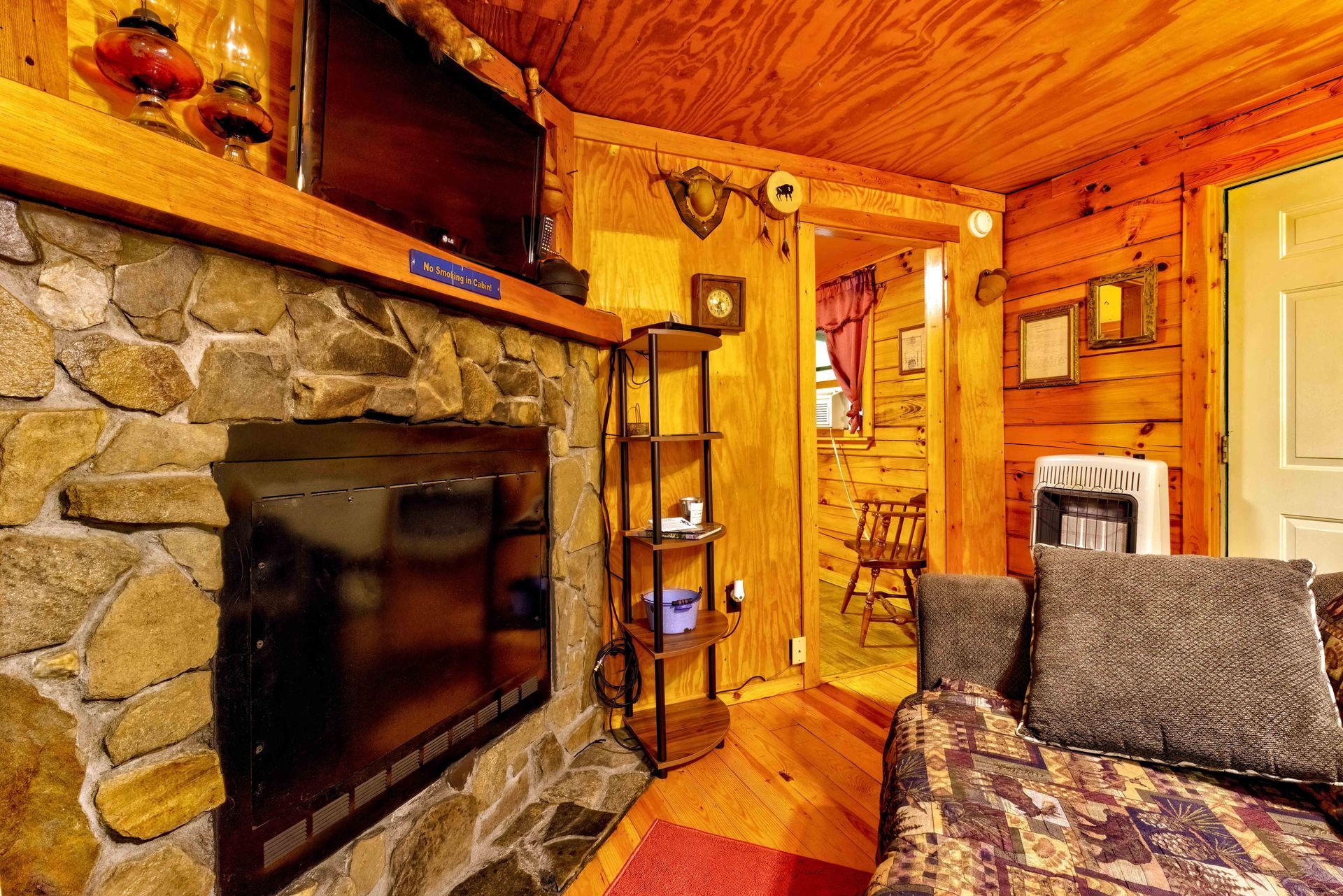 Cozy cabin living room with stone fireplace, wood-paneled walls, and patterned sofa in warm light