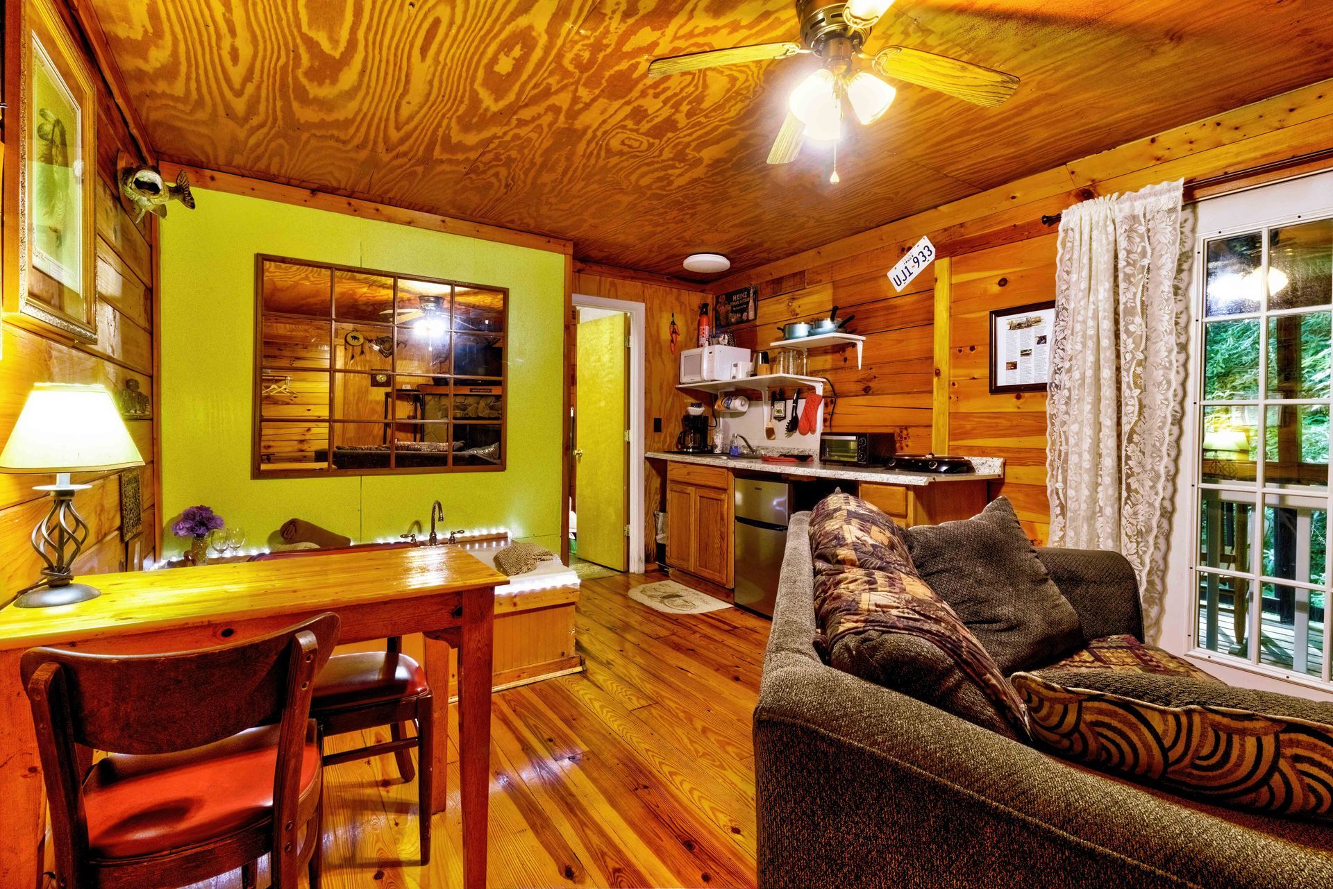 Cozy wood-paneled cabin interior with dining table, sofa, kitchen area, and glass doors to the outside