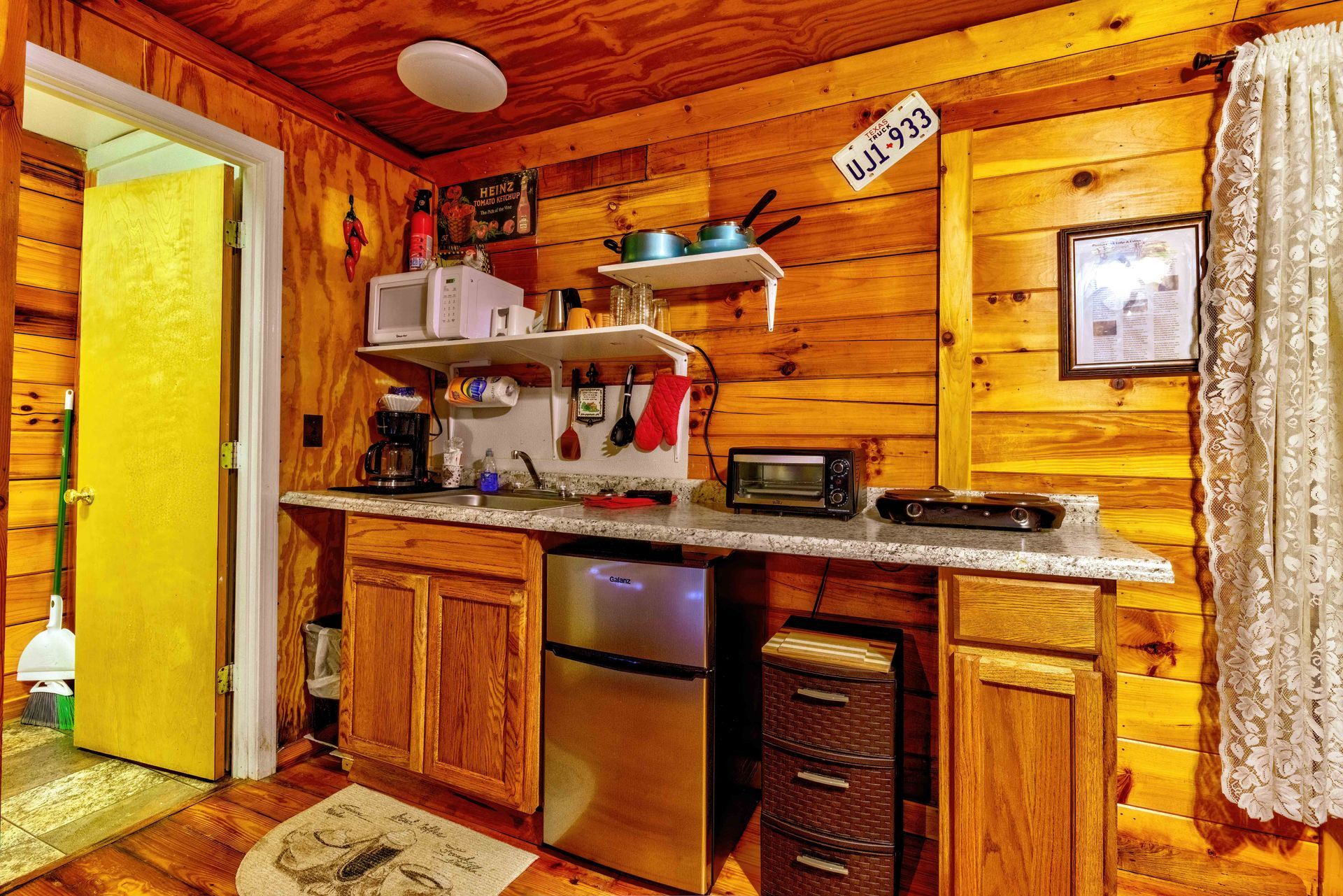 Wood-paneled rustic kitchen with wooden cabinets, counter appliances, and open doorway with yellow light