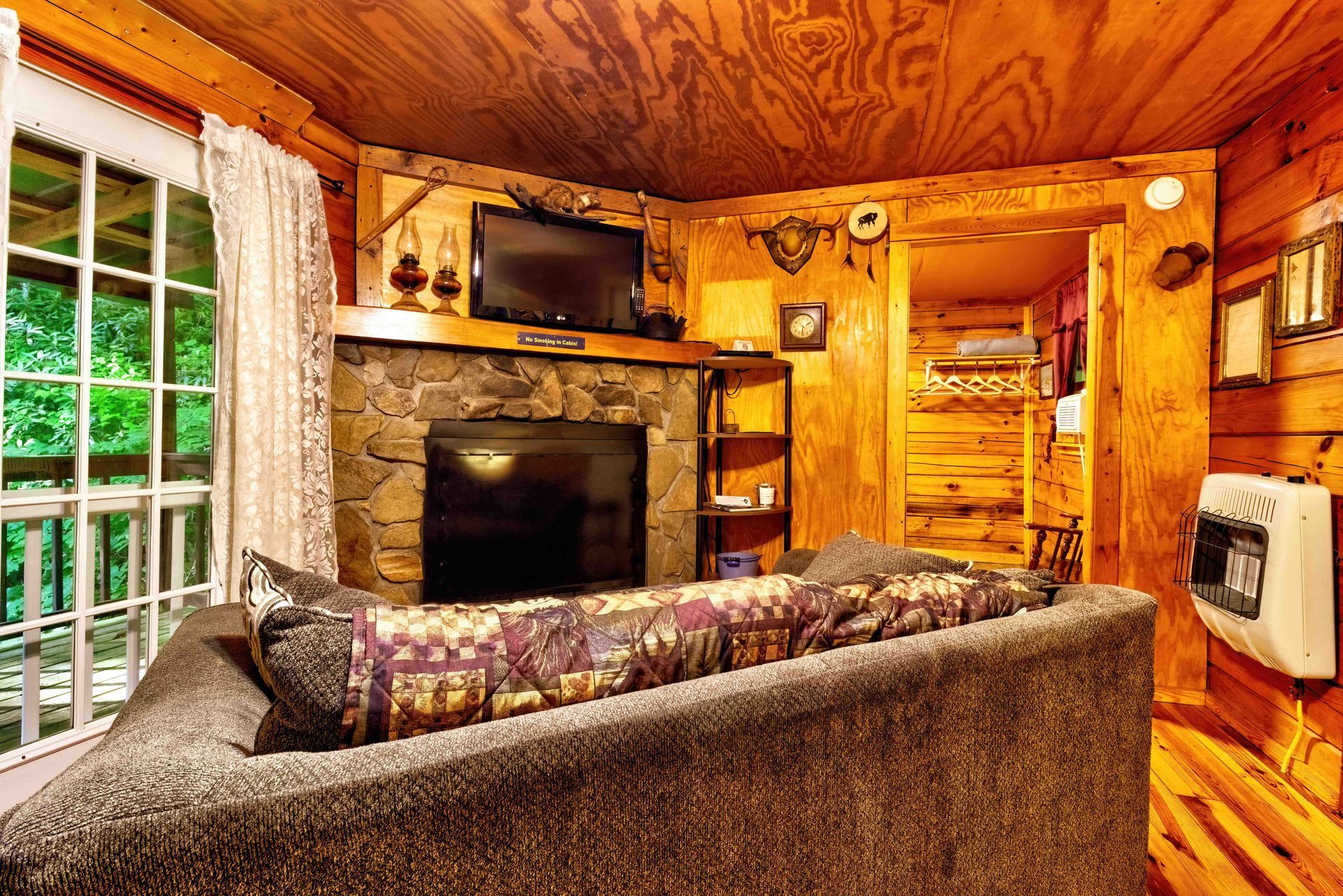 Cozy log cabin living room with stone fireplace, wood-paneled walls, and a sofa facing a TV.