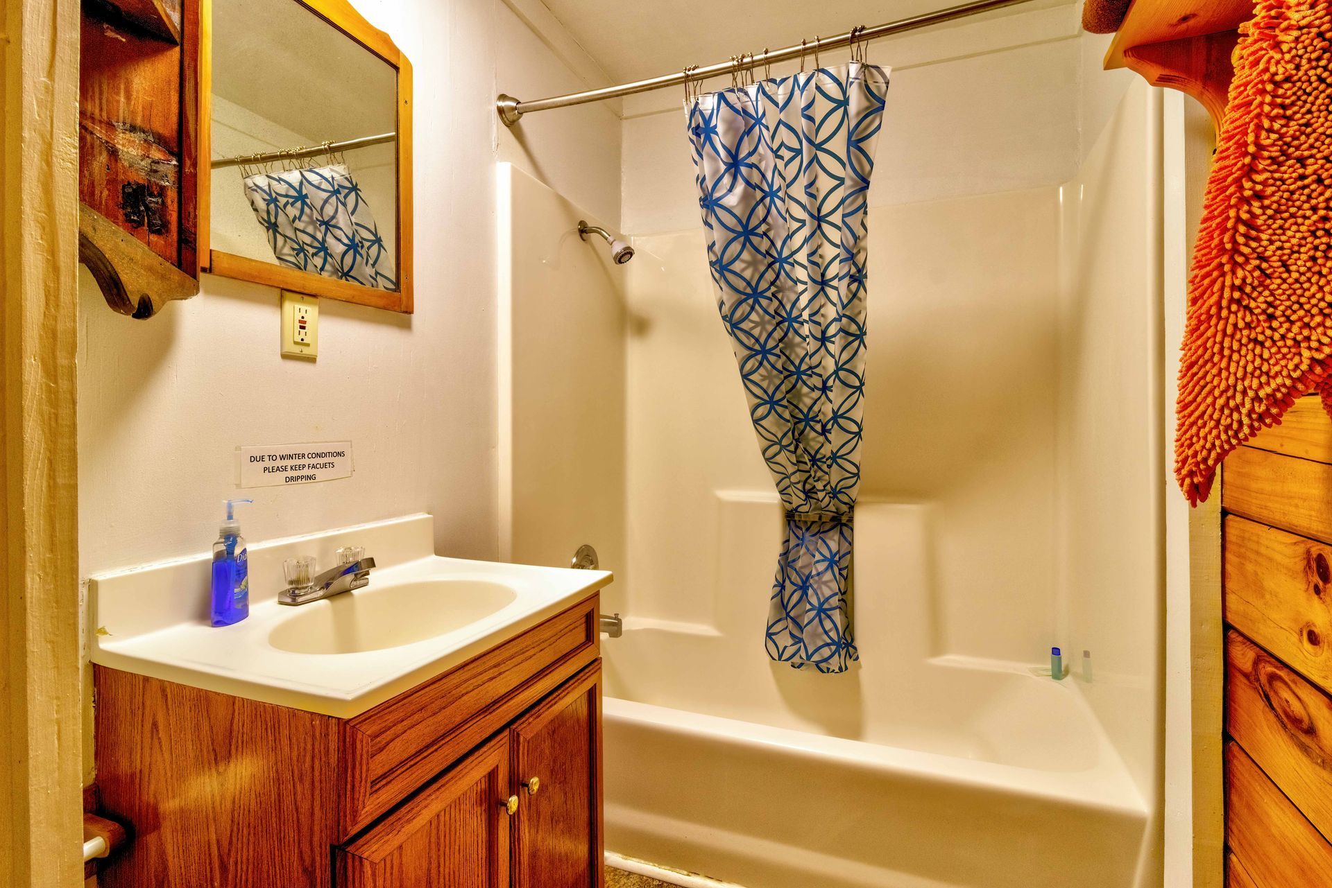 Small bathroom with wood vanity, white sink, bathtub, and patterned shower curtain.